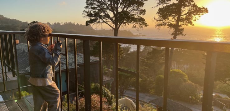 a child standing on a deck looking through a railing at the sunset