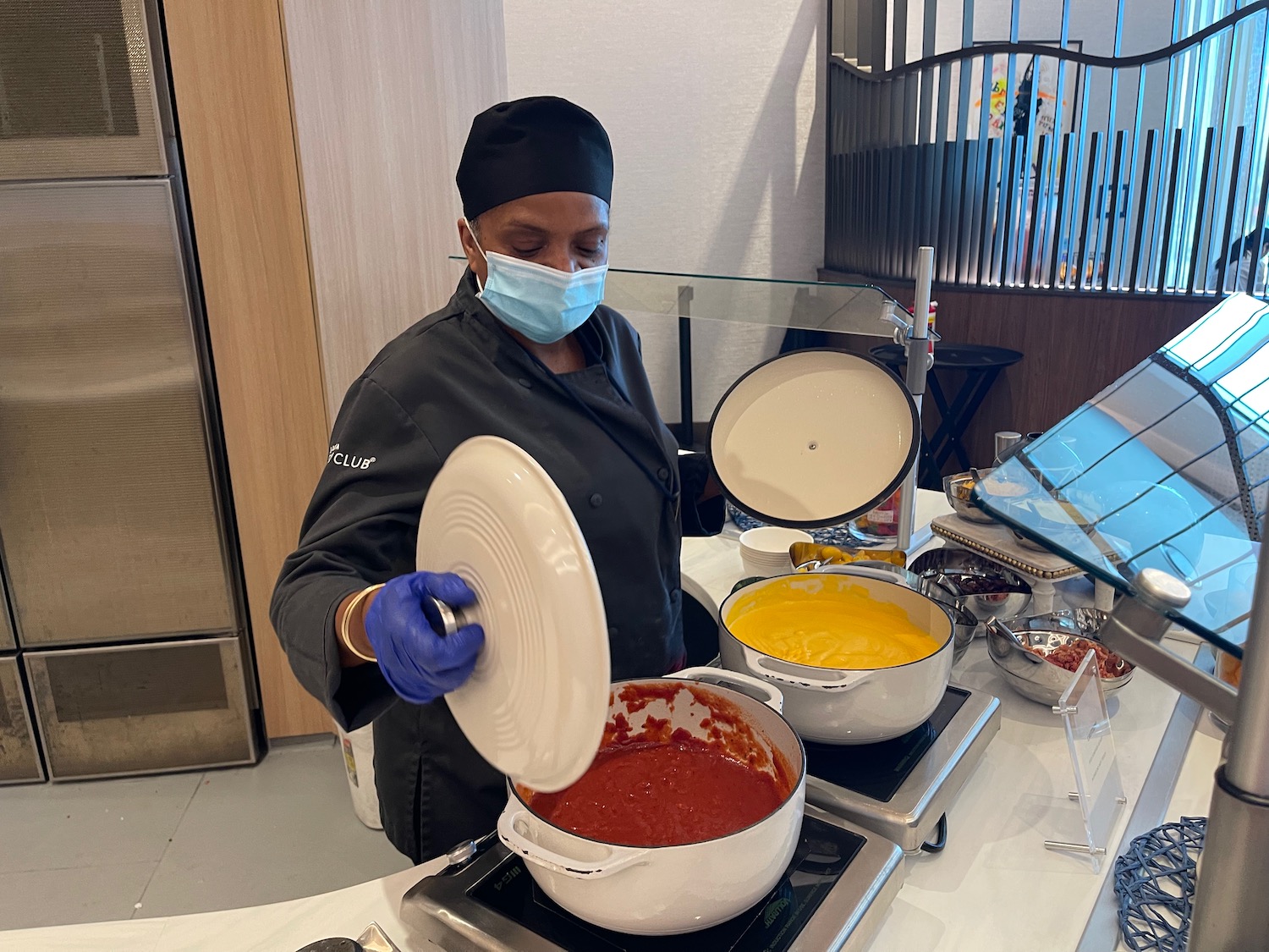 a woman wearing a face mask and gloves pouring sauce into a pan