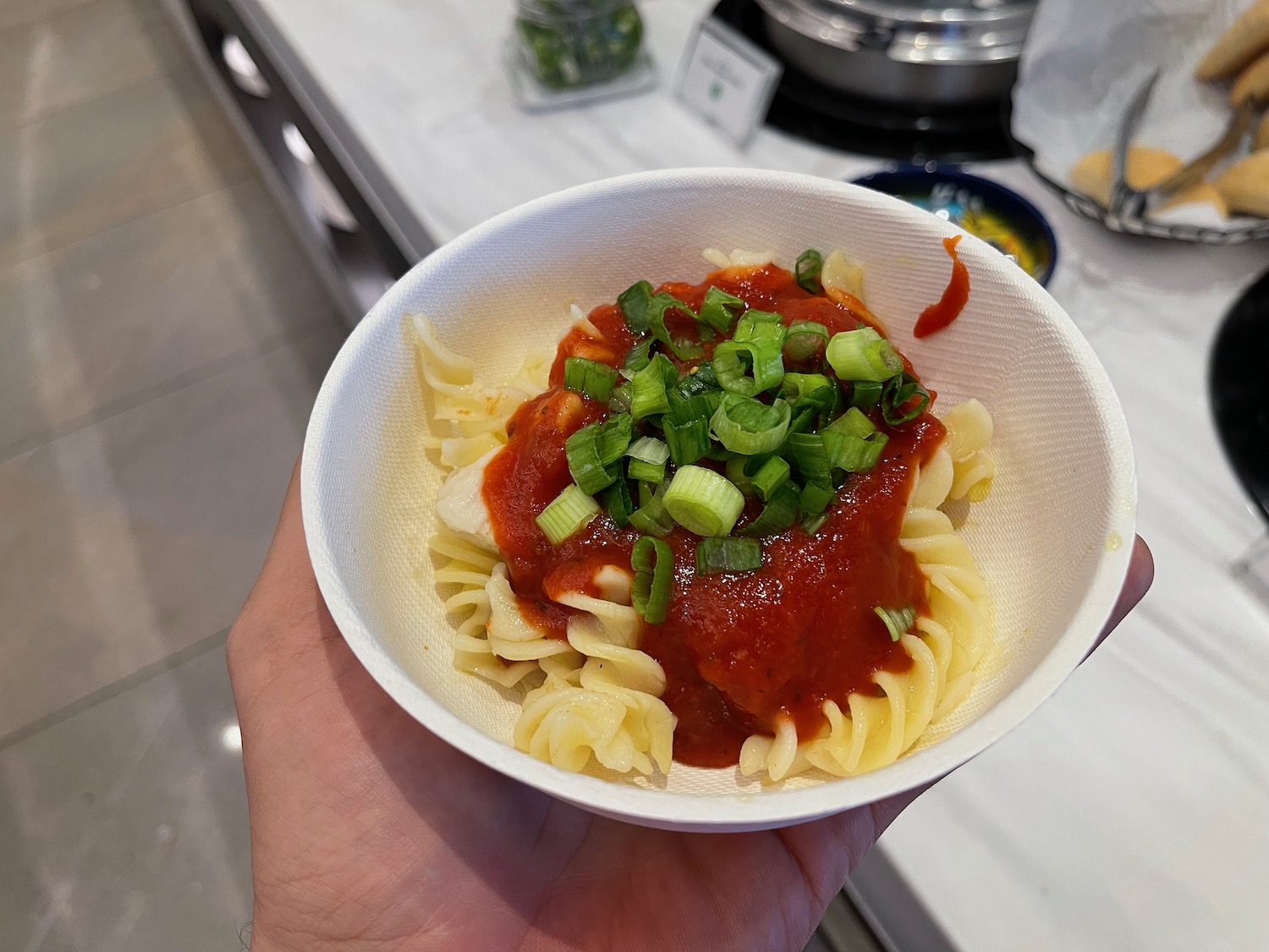 a hand holding a bowl of pasta with sauce and green onions