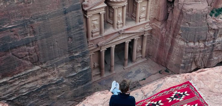 a person sitting on a red rug looking at a building in a canyon