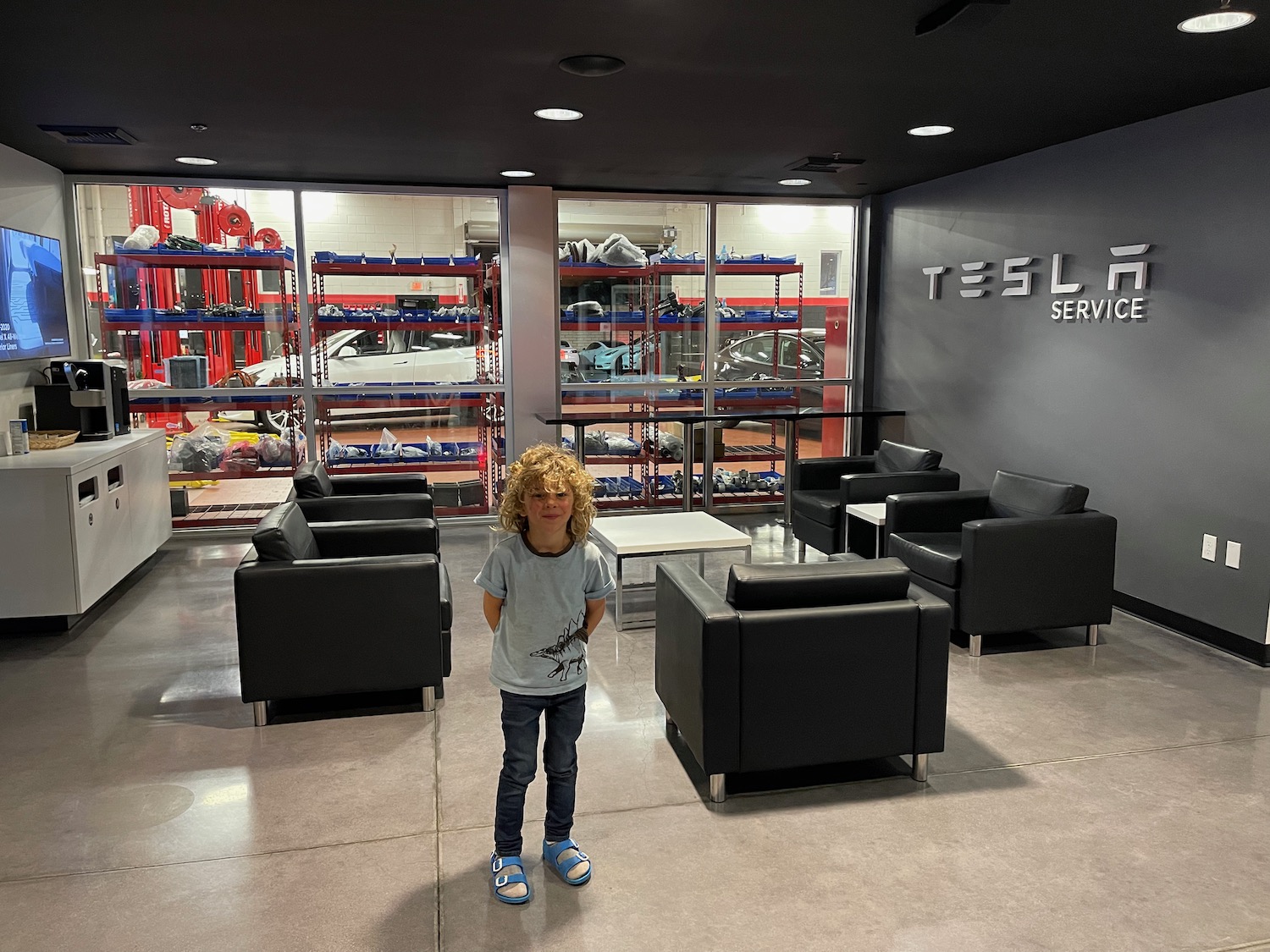 a boy standing in a room with black chairs and a black wall