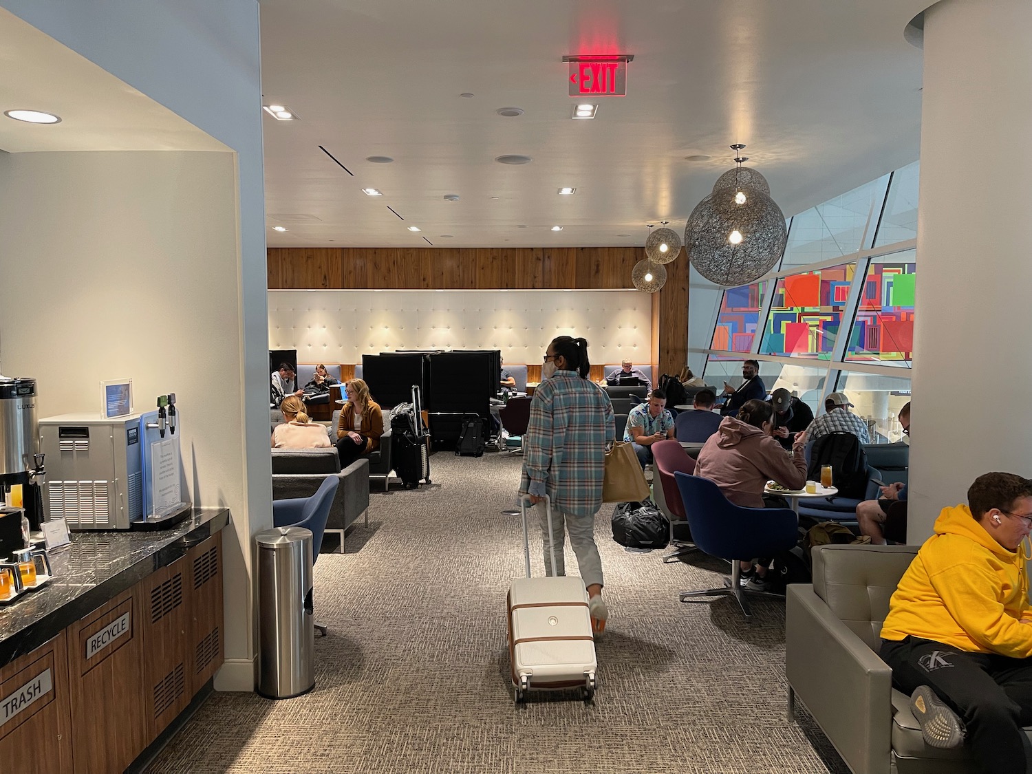 a woman walking with luggage in a room with people sitting around