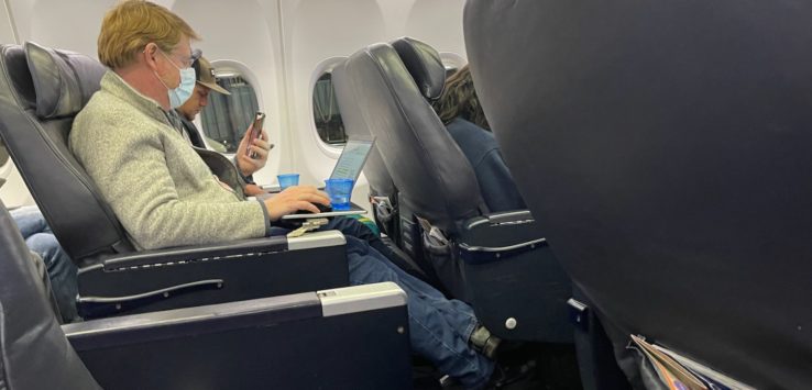people sitting in an airplane with a laptop and a man wearing a face mask