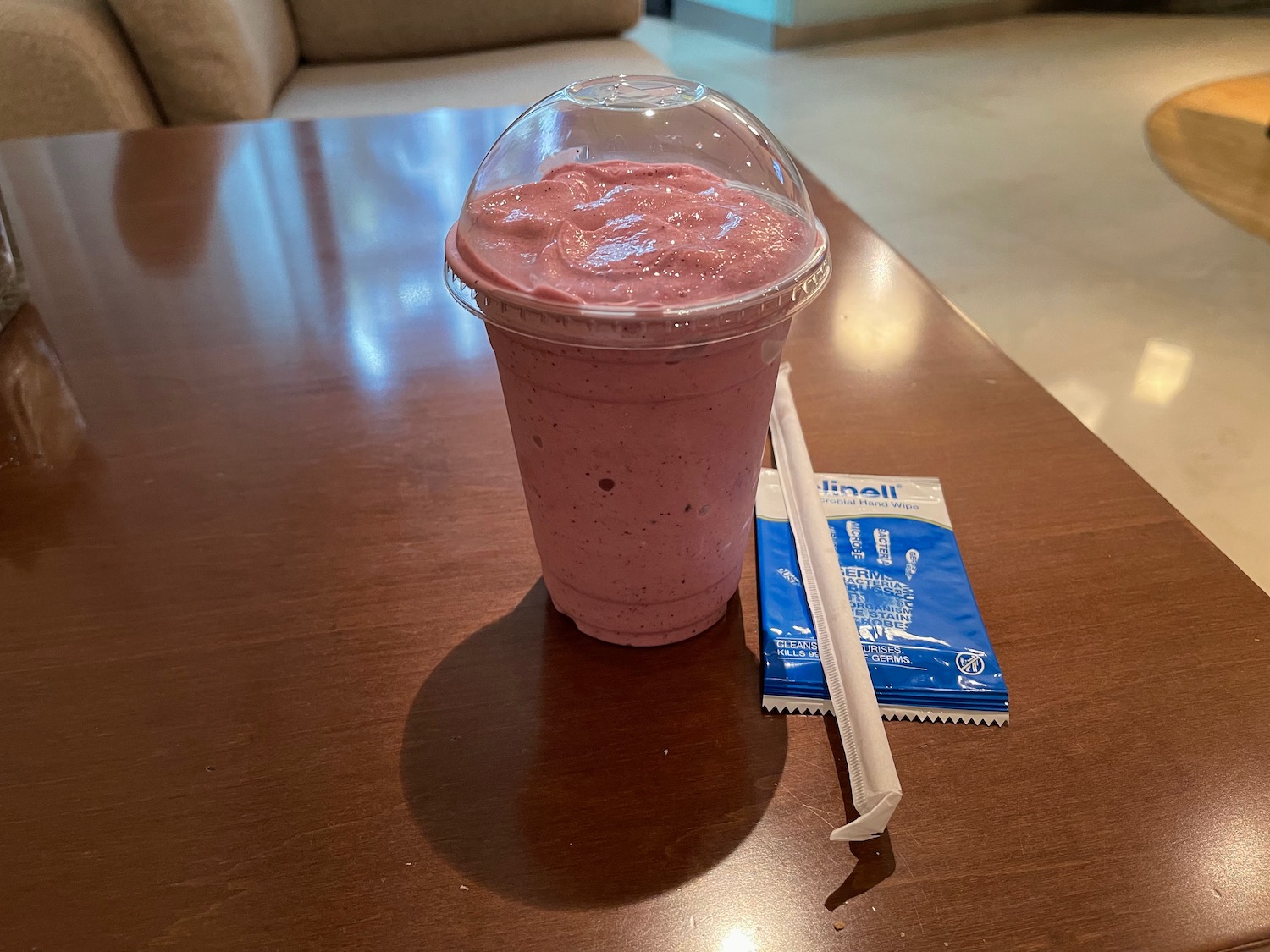 a pink smoothie in a plastic cup with straw and a packet on a table