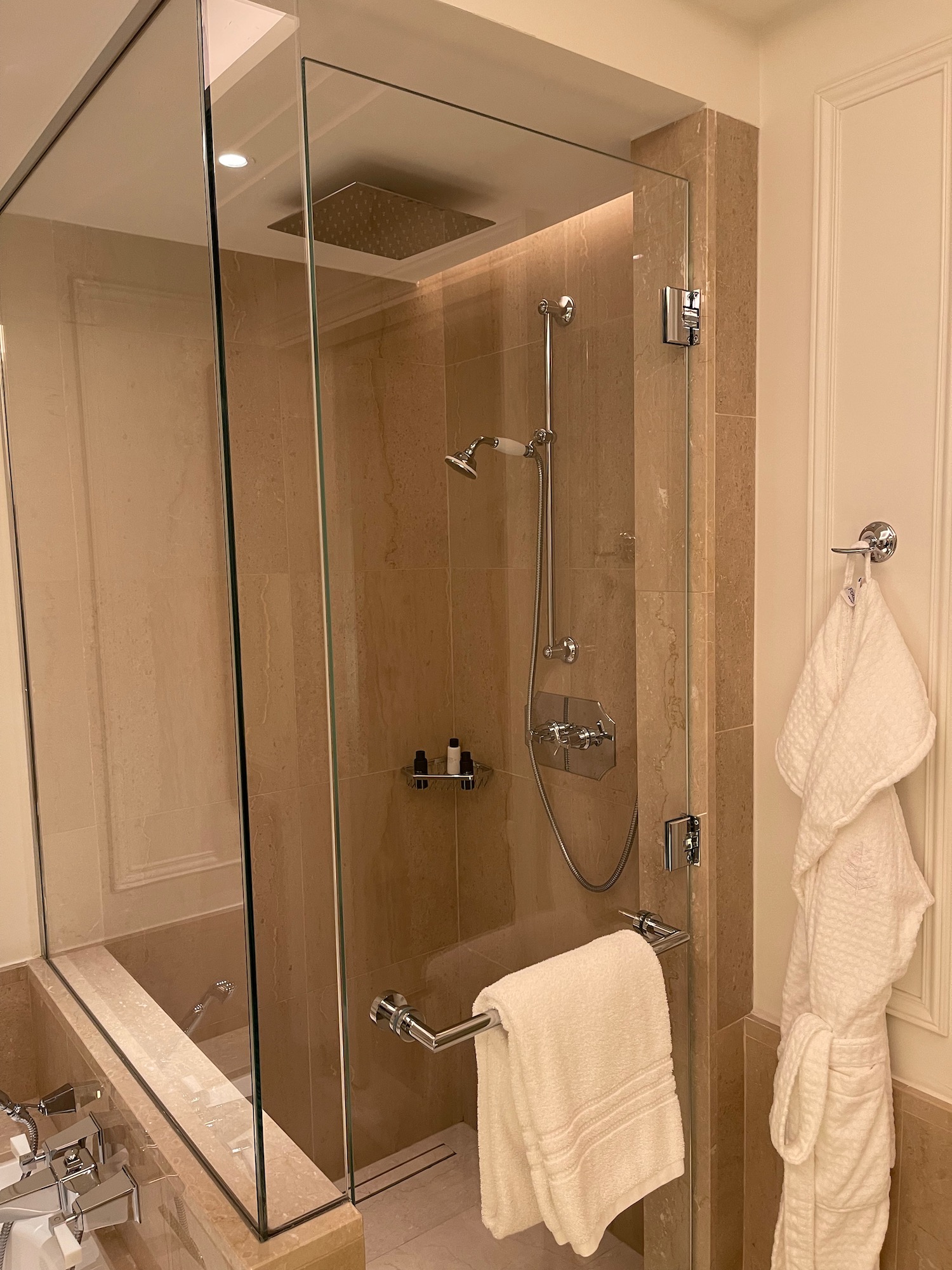 a glass shower with a bathtub and a towel on the wall