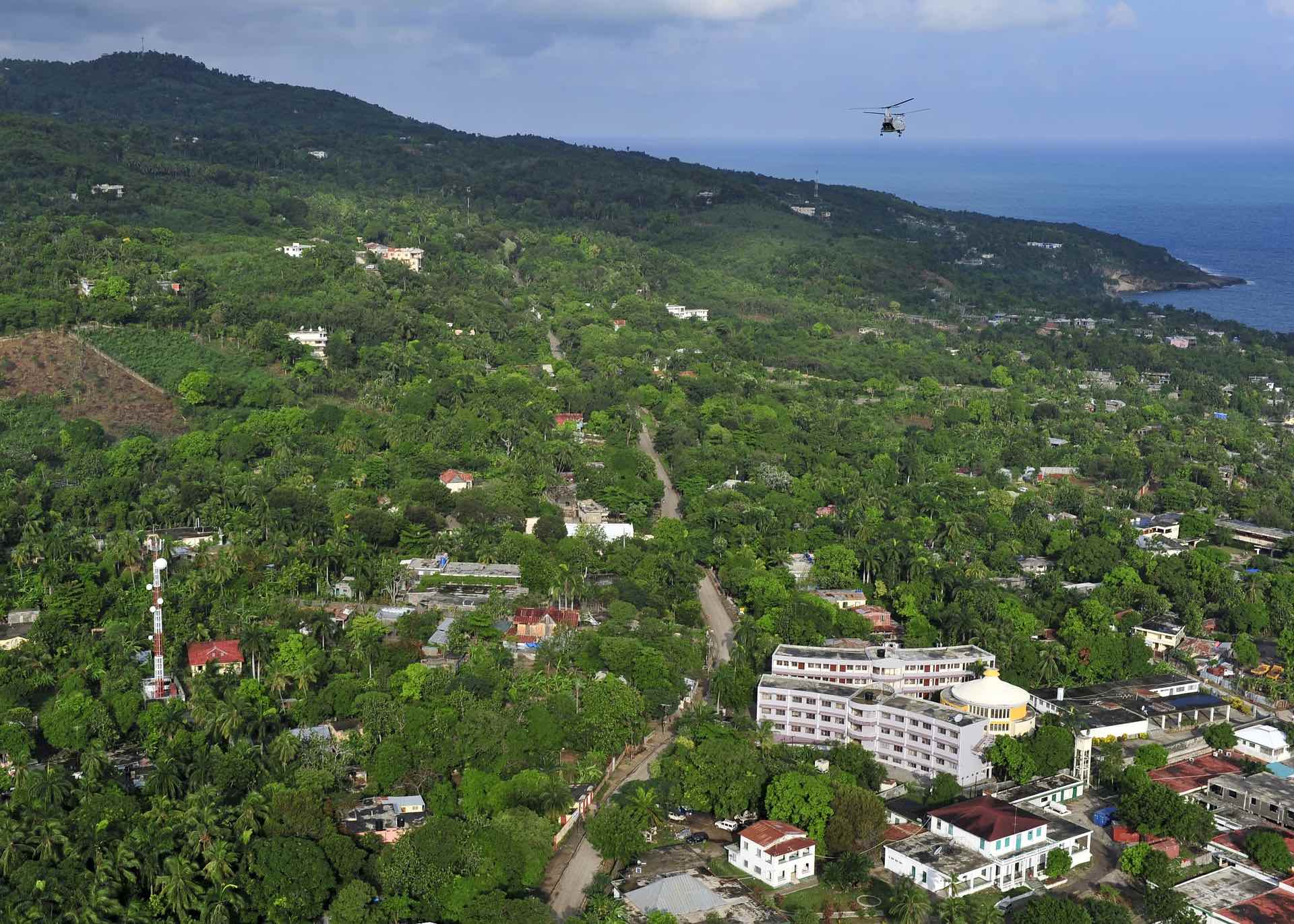 a helicopter flying over a green hill with trees