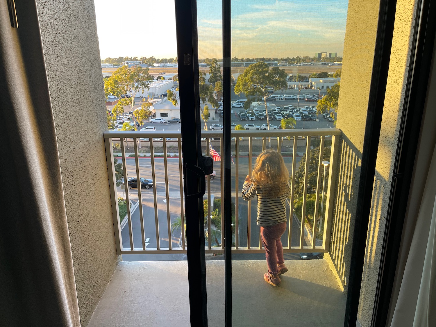 a child standing on a balcony looking out to a parking lot
