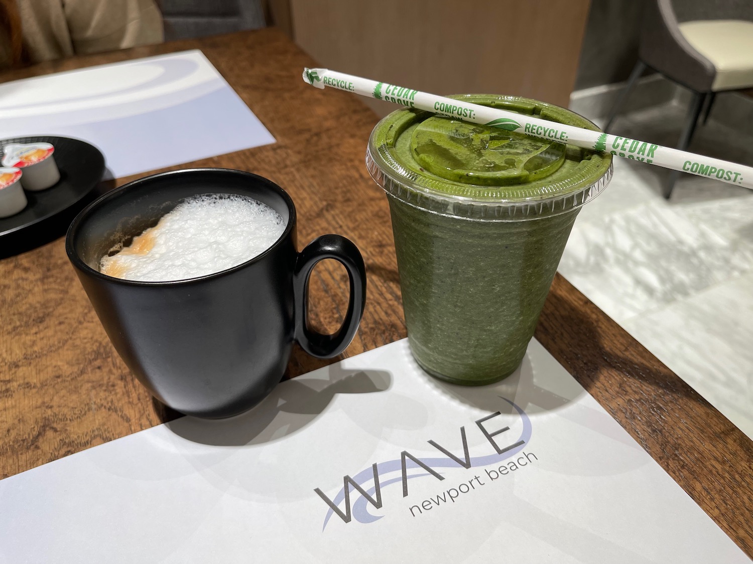 a green drink in a plastic cup next to a black mug with a straw