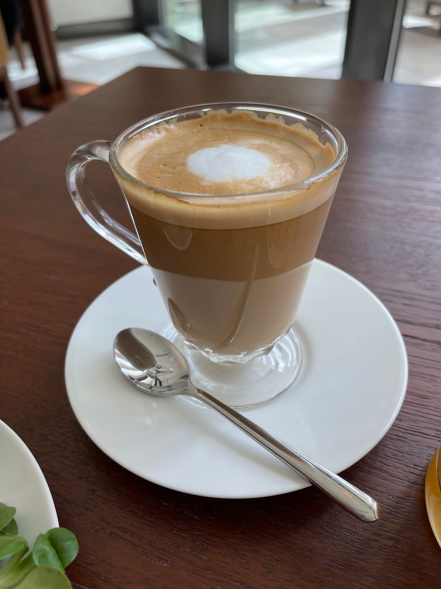 a glass cup of coffee on a plate with a spoon