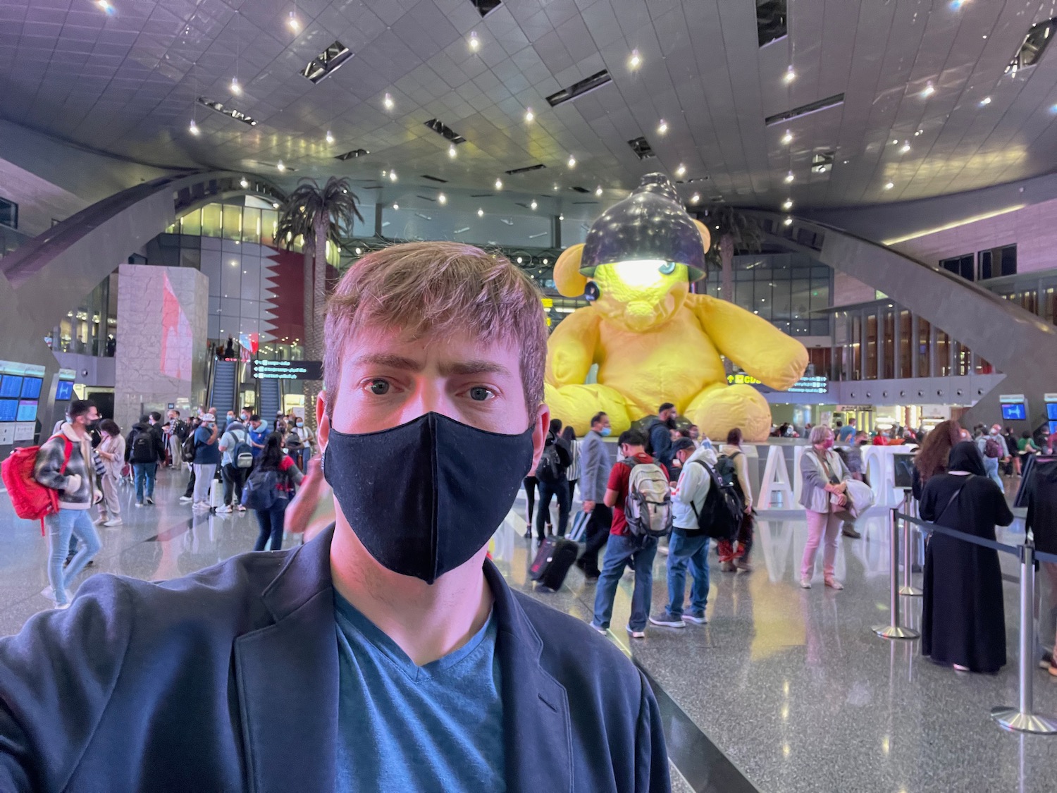 a man taking a selfie in a large building with a large yellow stuffed bear
