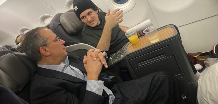 a man in a suit and hat talking to a man on an airplane