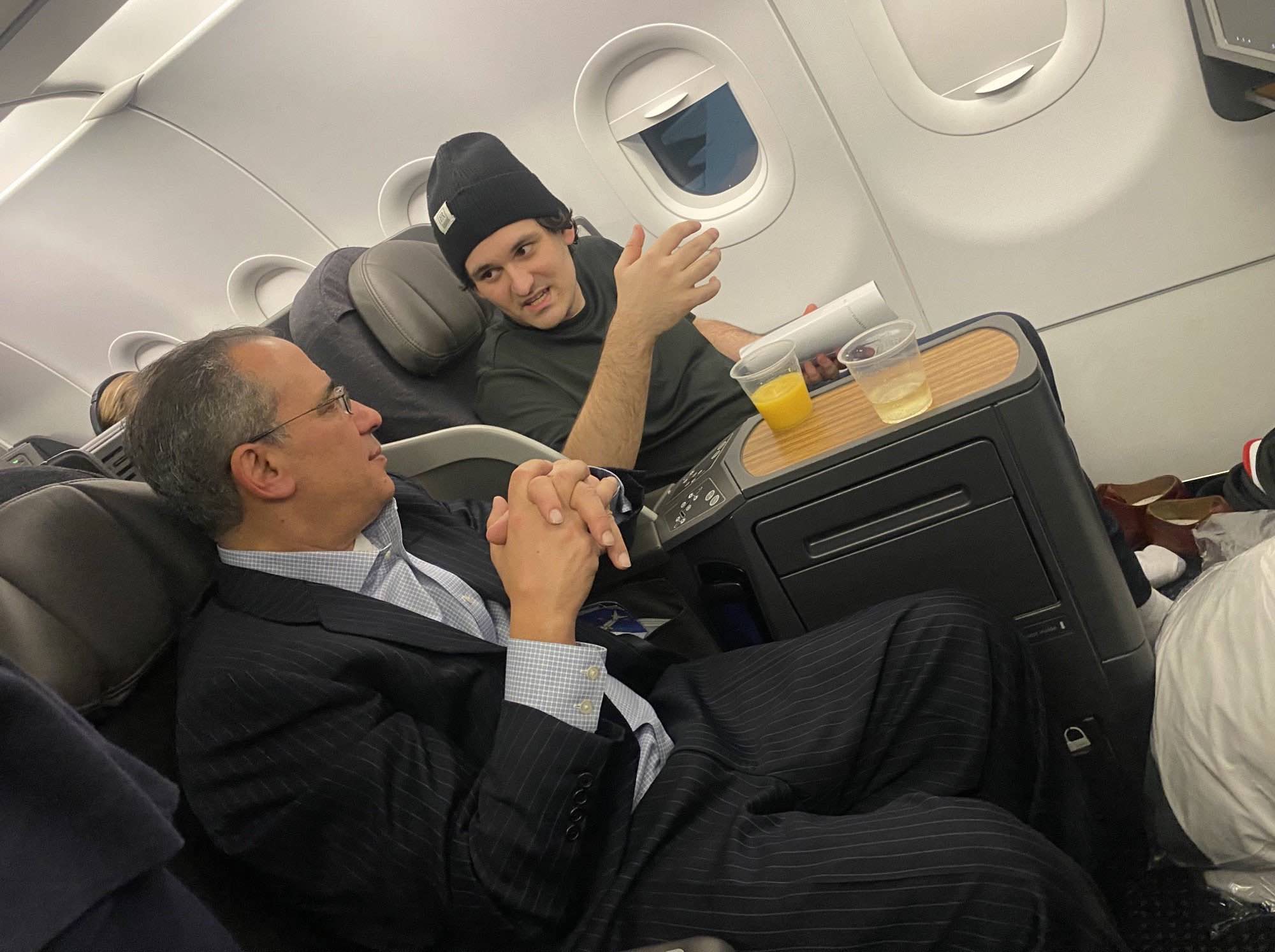 a man in a suit and hat talking to a man on an airplane