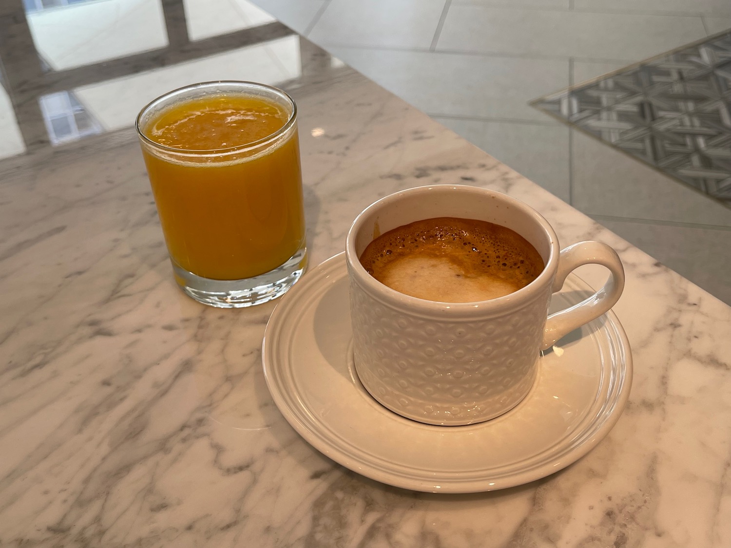 a cup of coffee and a glass of orange juice on a marble table