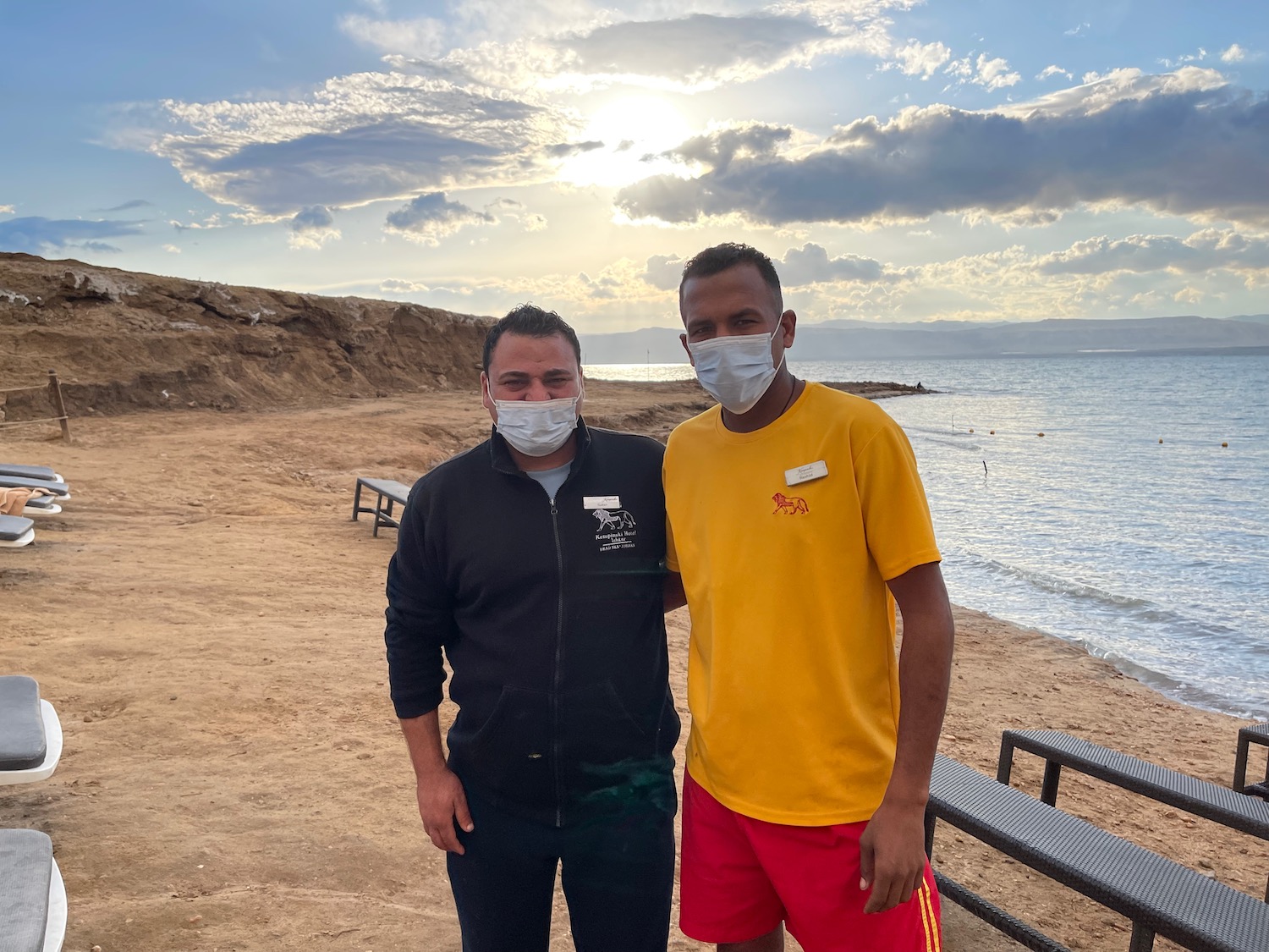 two men wearing face masks on a beach