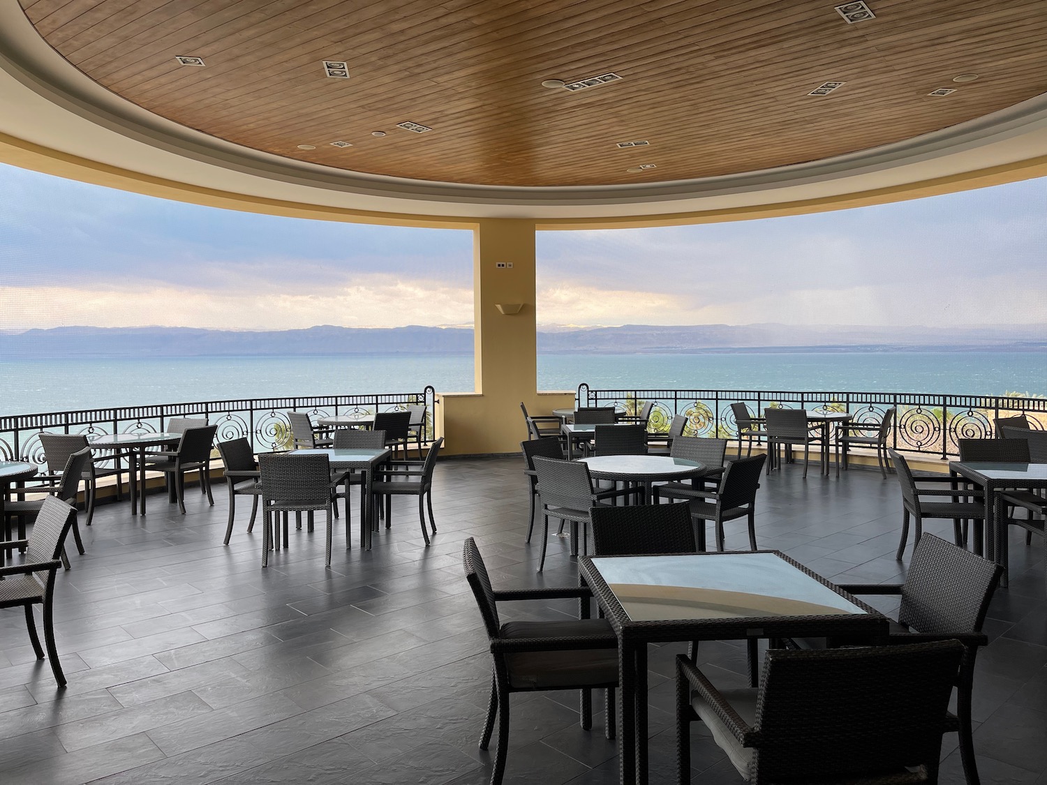 a room with tables and chairs and a railing overlooking the ocean