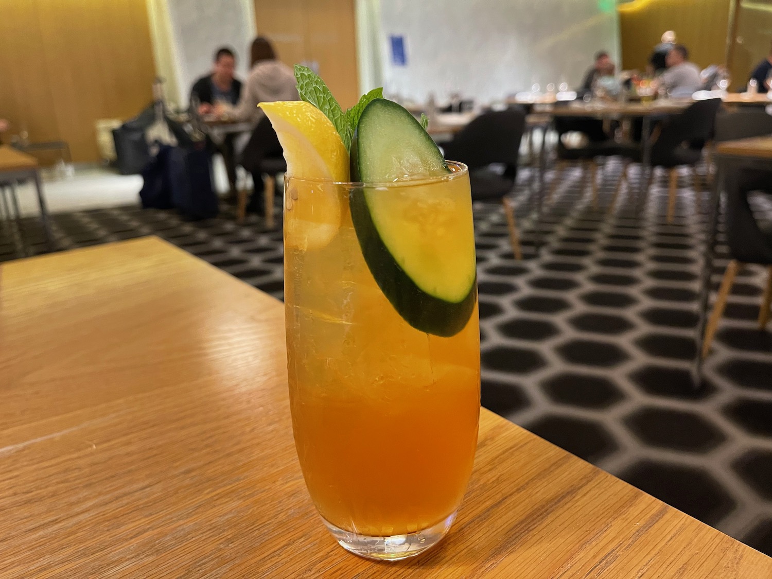 a glass of orange liquid with cucumber slices and mint on a table