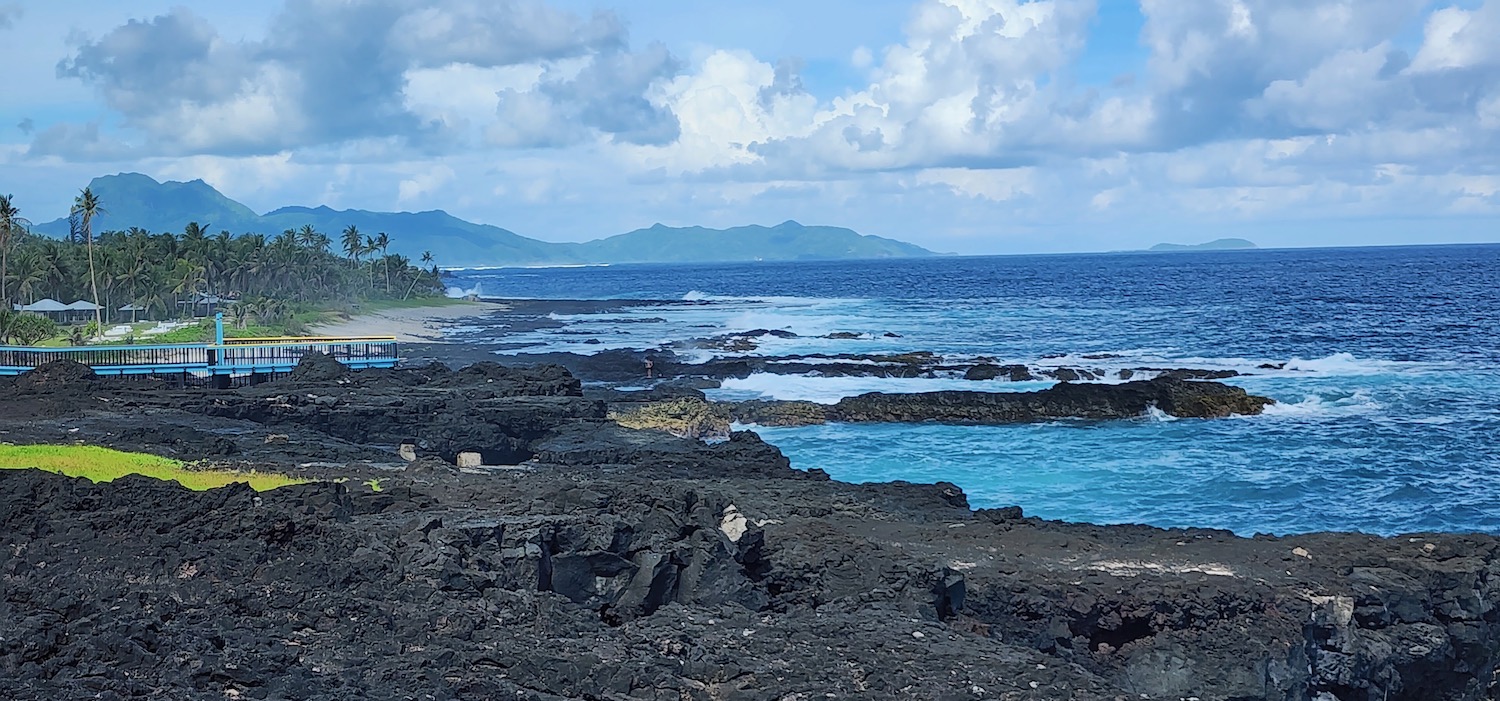 a rocky beach with blue water and mountains in the background