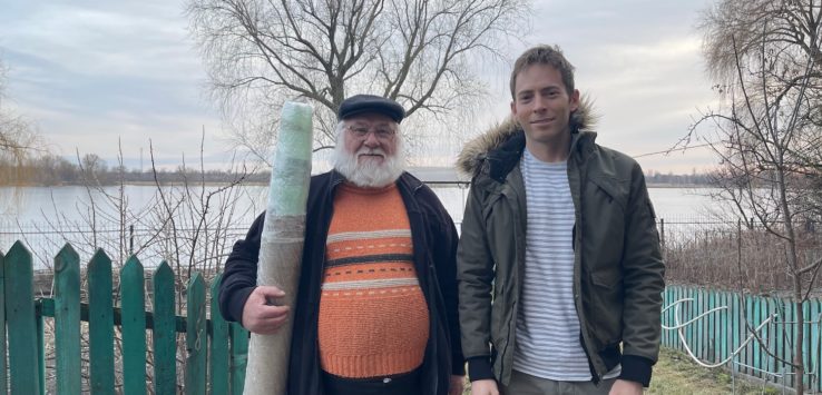 a man holding a pole next to a man standing next to a fence