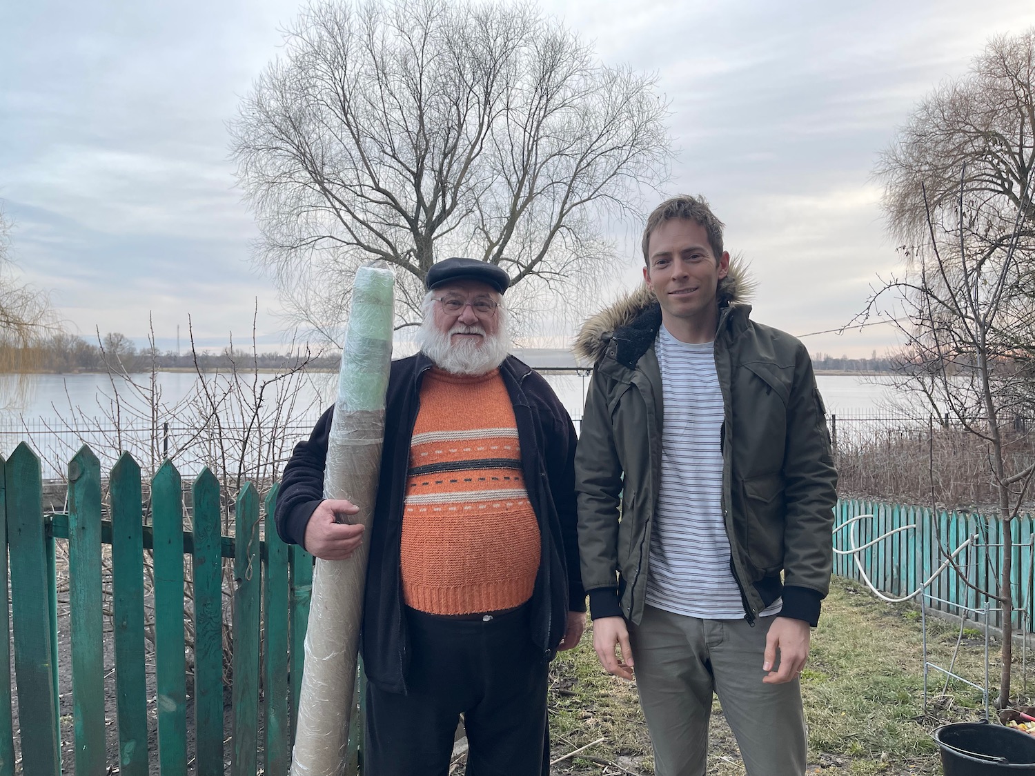 a man holding a pole next to a man standing next to a fence