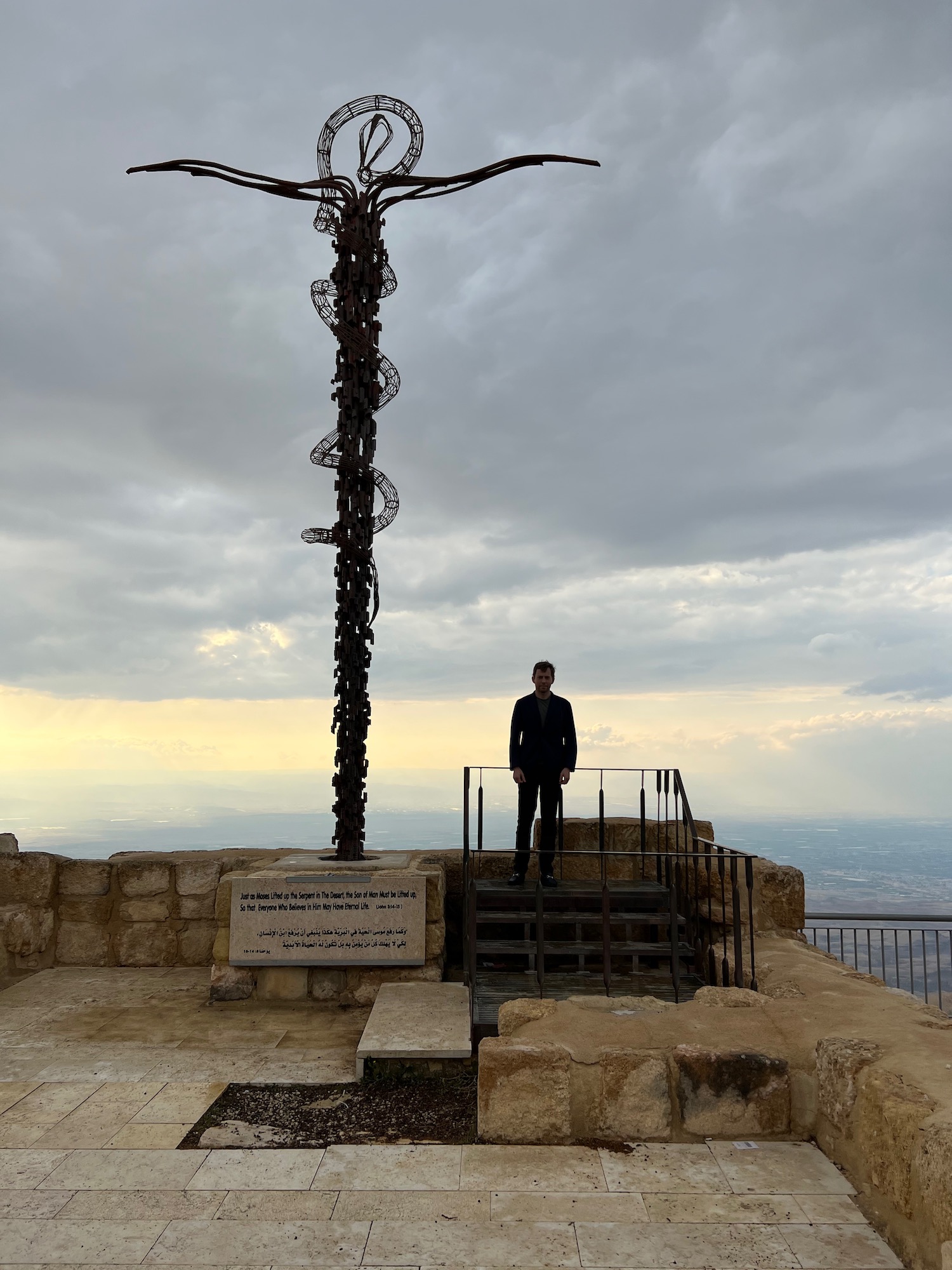 a man standing on a stone ledge with a statue of a cross