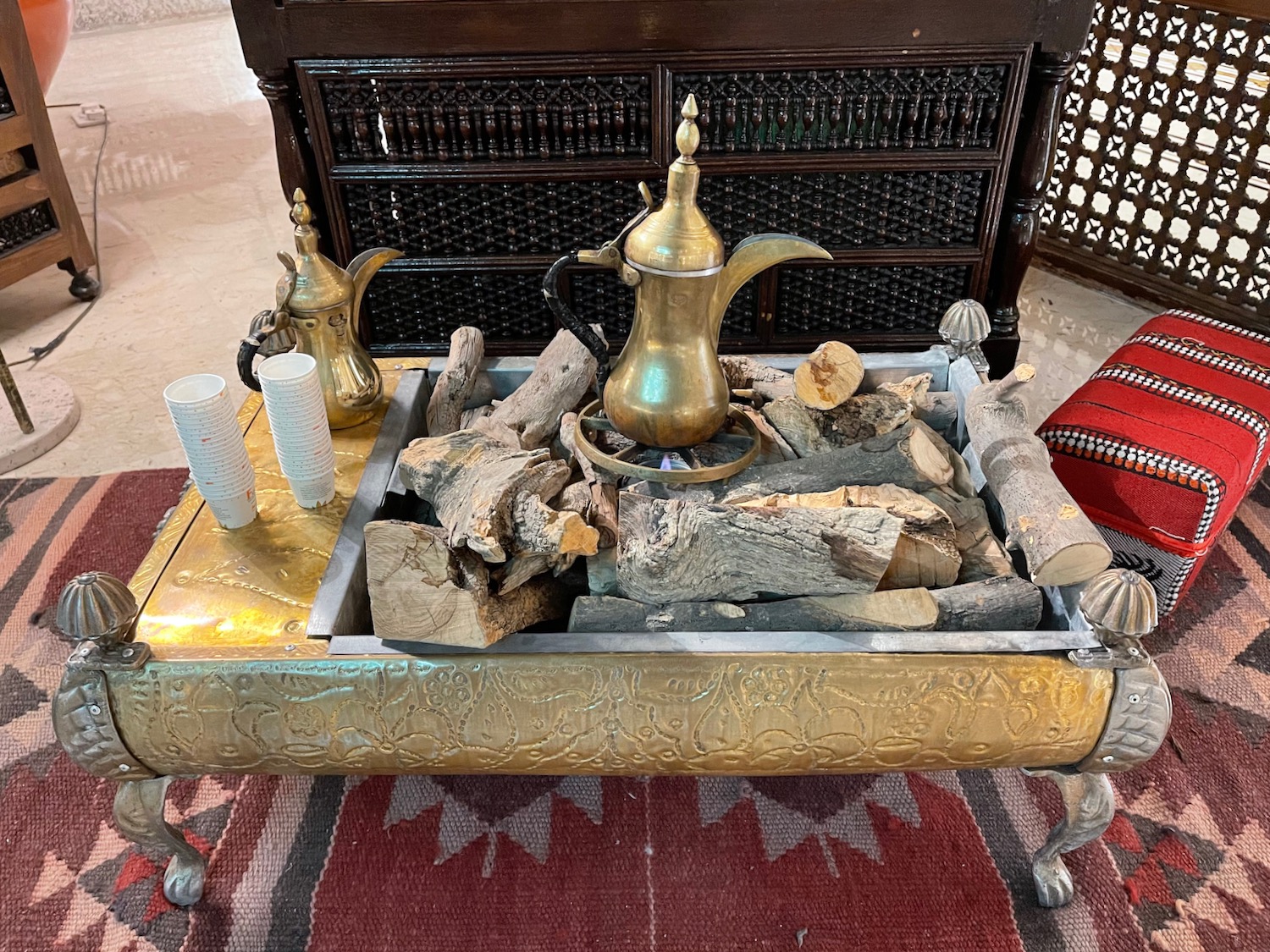 a gold and silver coffee pot with wood and cups on a table