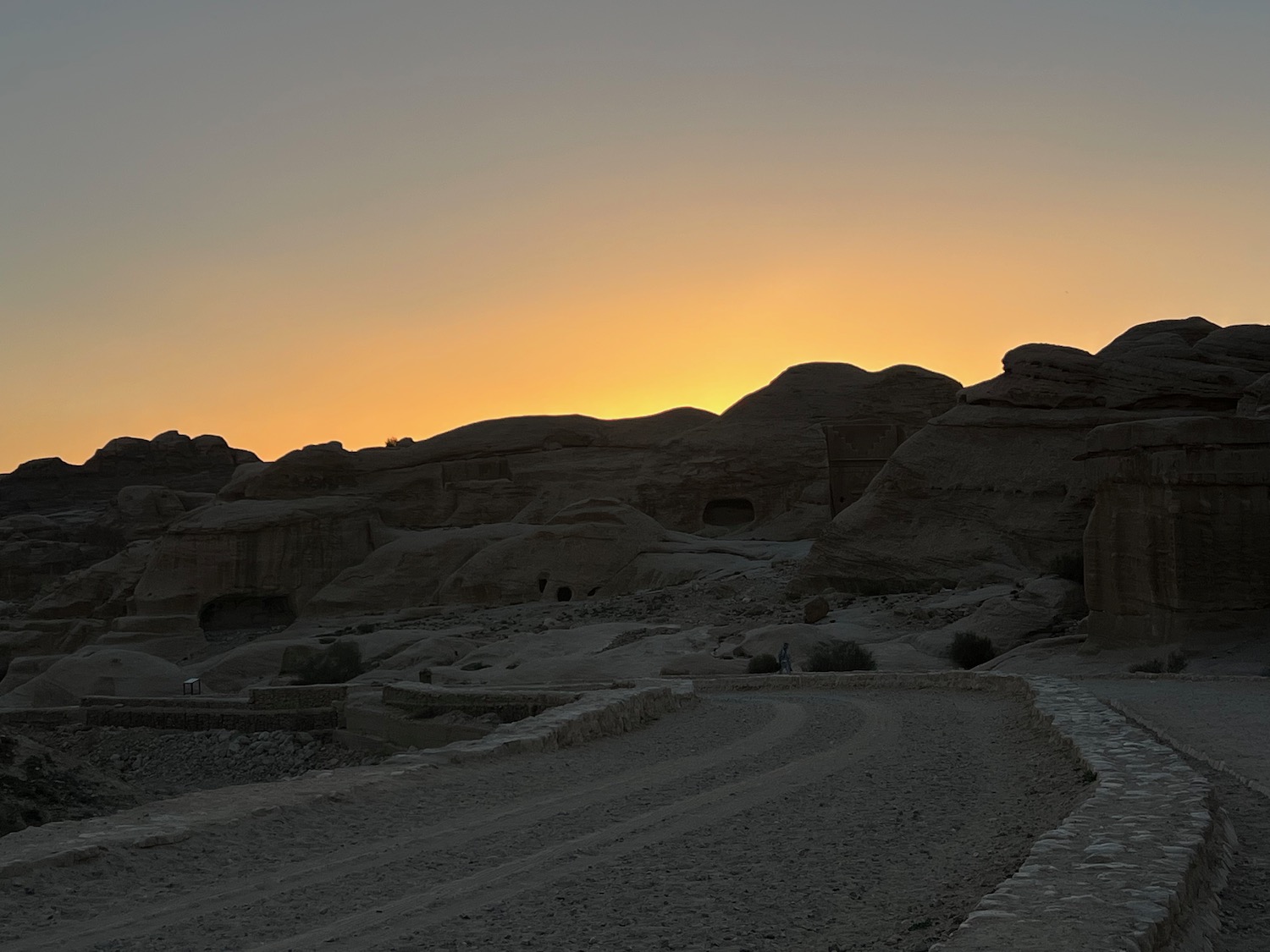 a dirt road with a large rock formation in the background