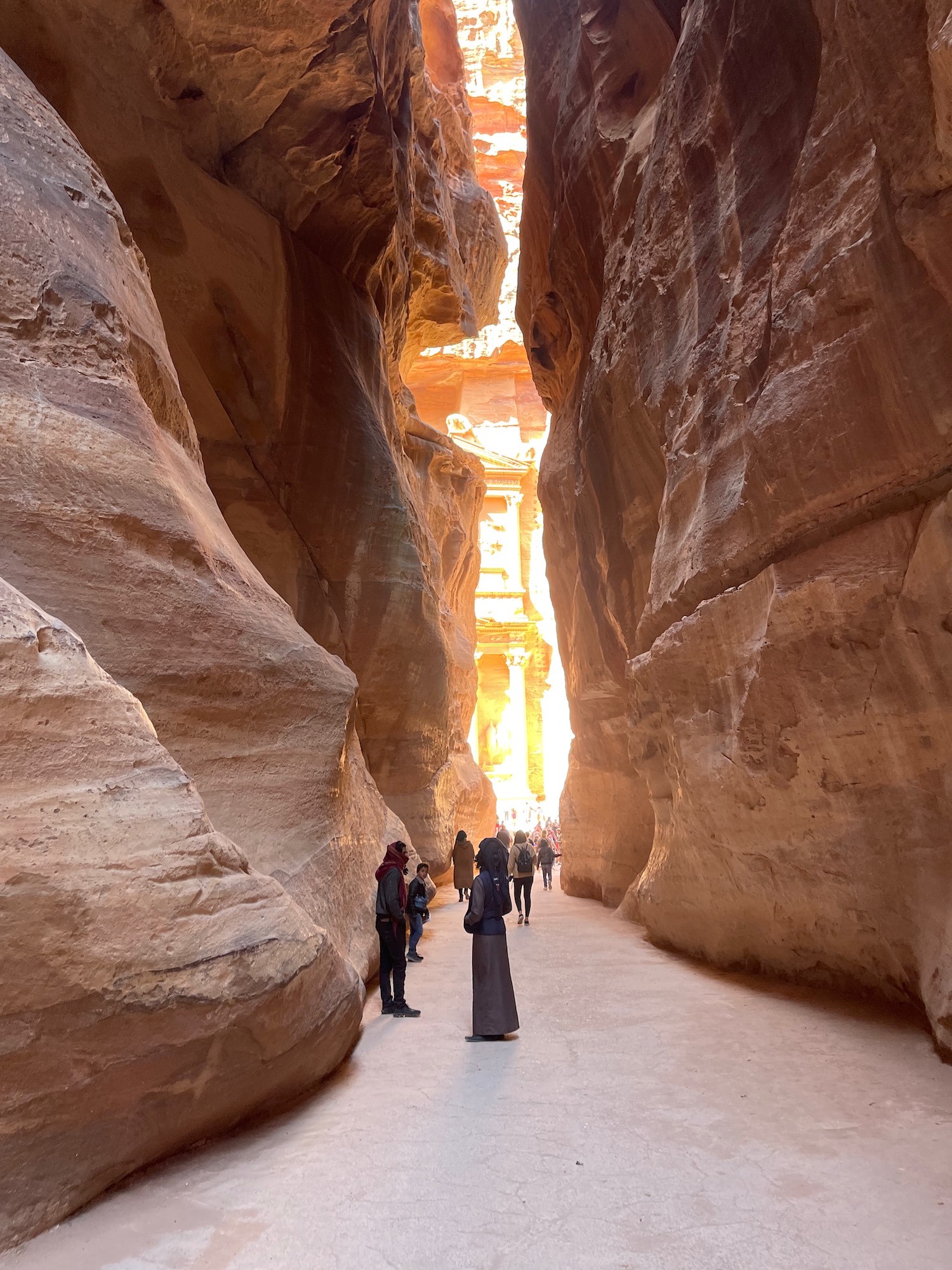 a group of people walking through a narrow canyon with Petra in the background