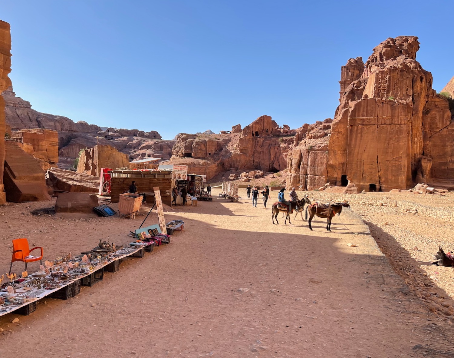 a group of people walking on a dirt road with horses and a few people