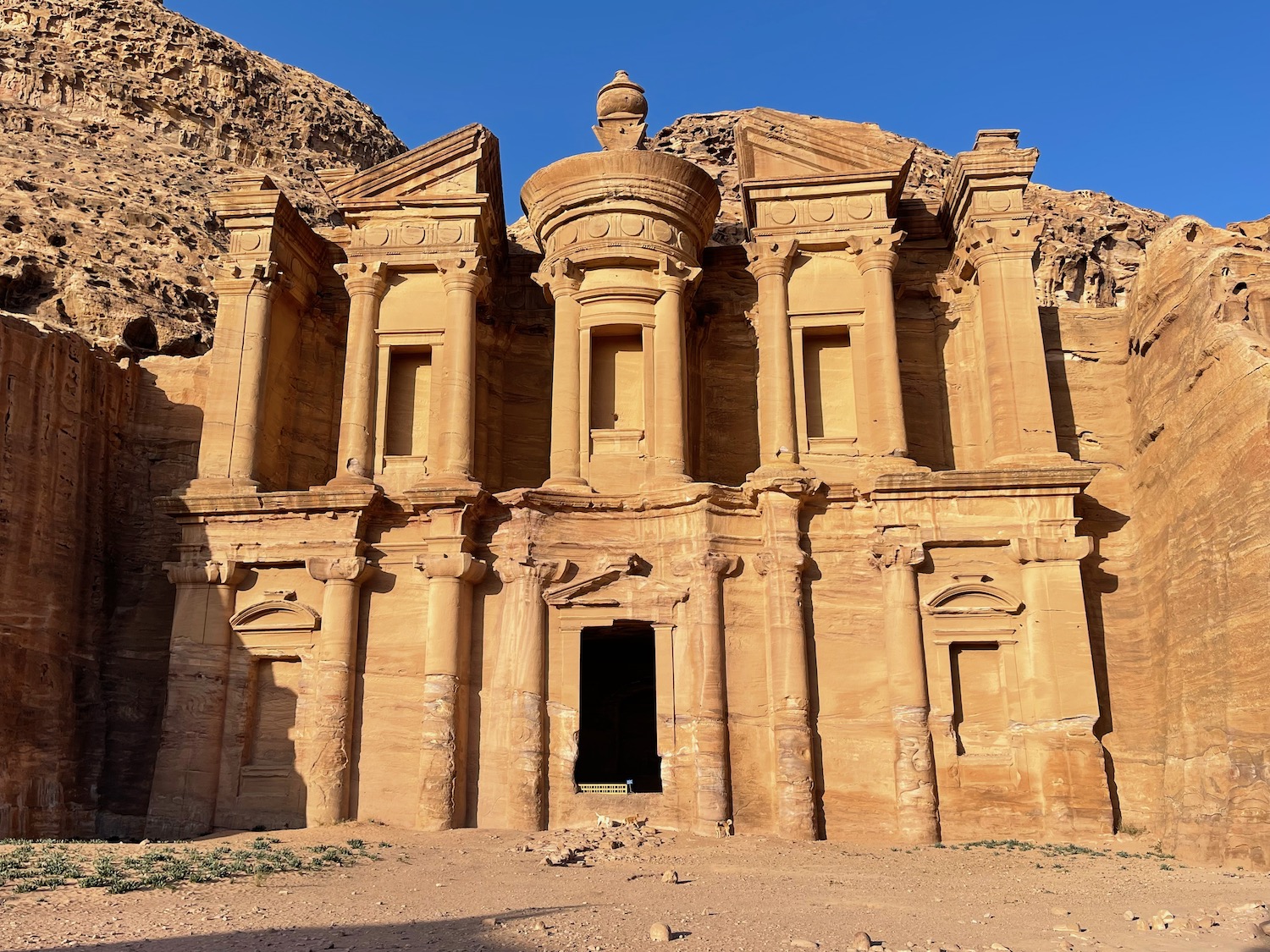 a stone building with columns and a rock formation with Petra in the background