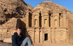 a man sitting on a rock in front of a stone building with Petra in the background