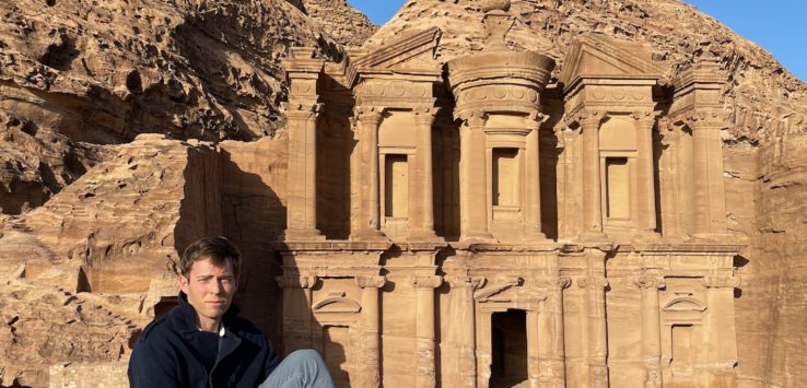 a man sitting on a rock in front of a stone building with Petra in the background