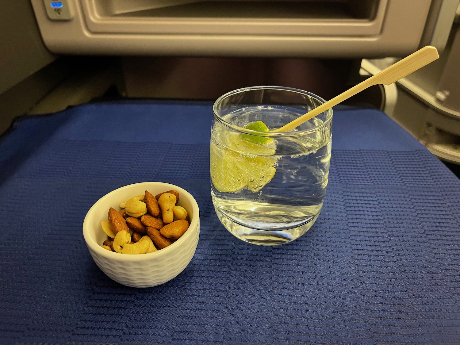 a glass of water with a lemon slice and a bowl of nuts