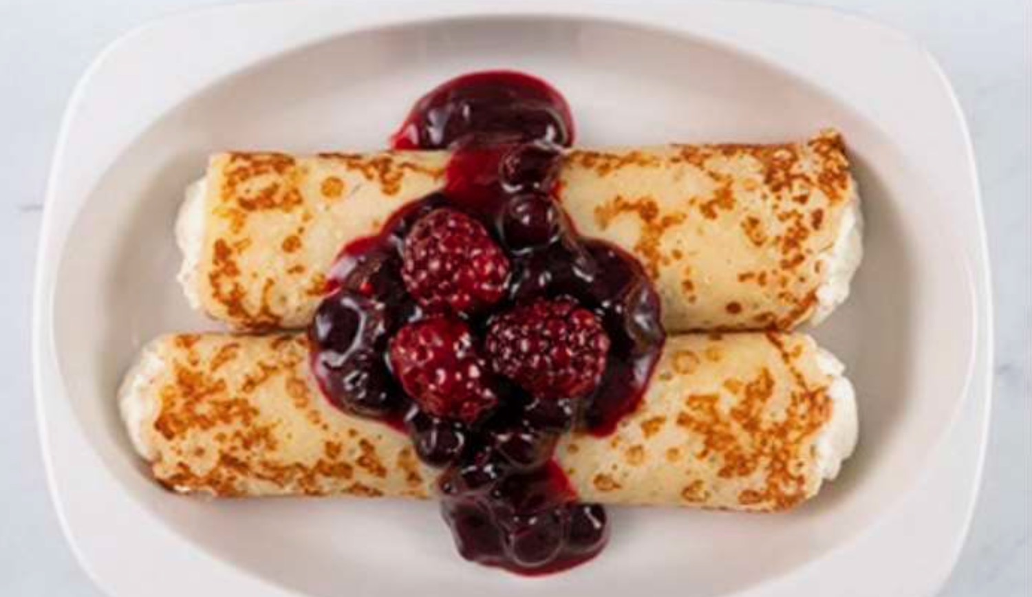 a plate of crepes with berries and jam