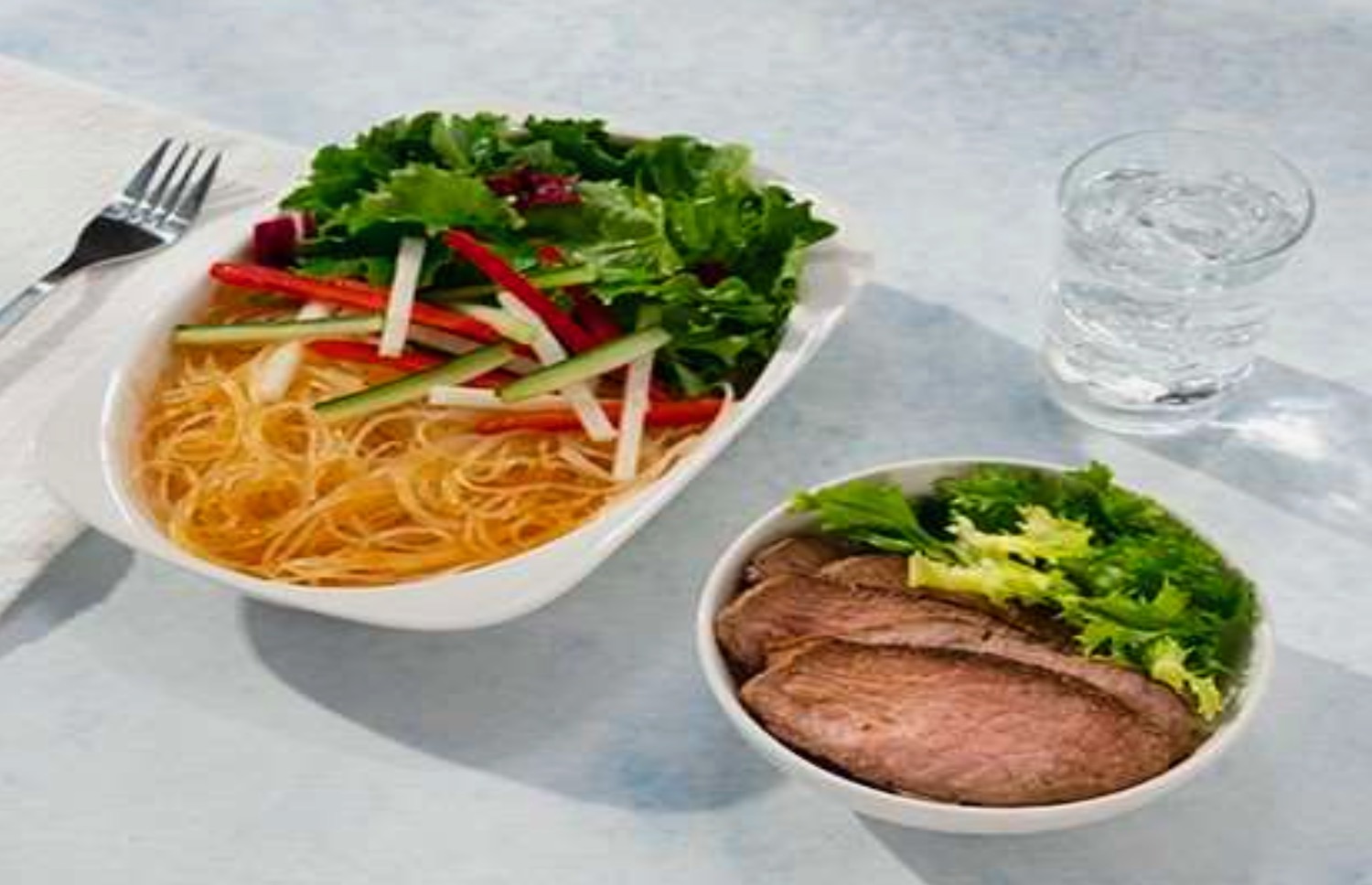 a plate of noodles and vegetables in a bowl of meat