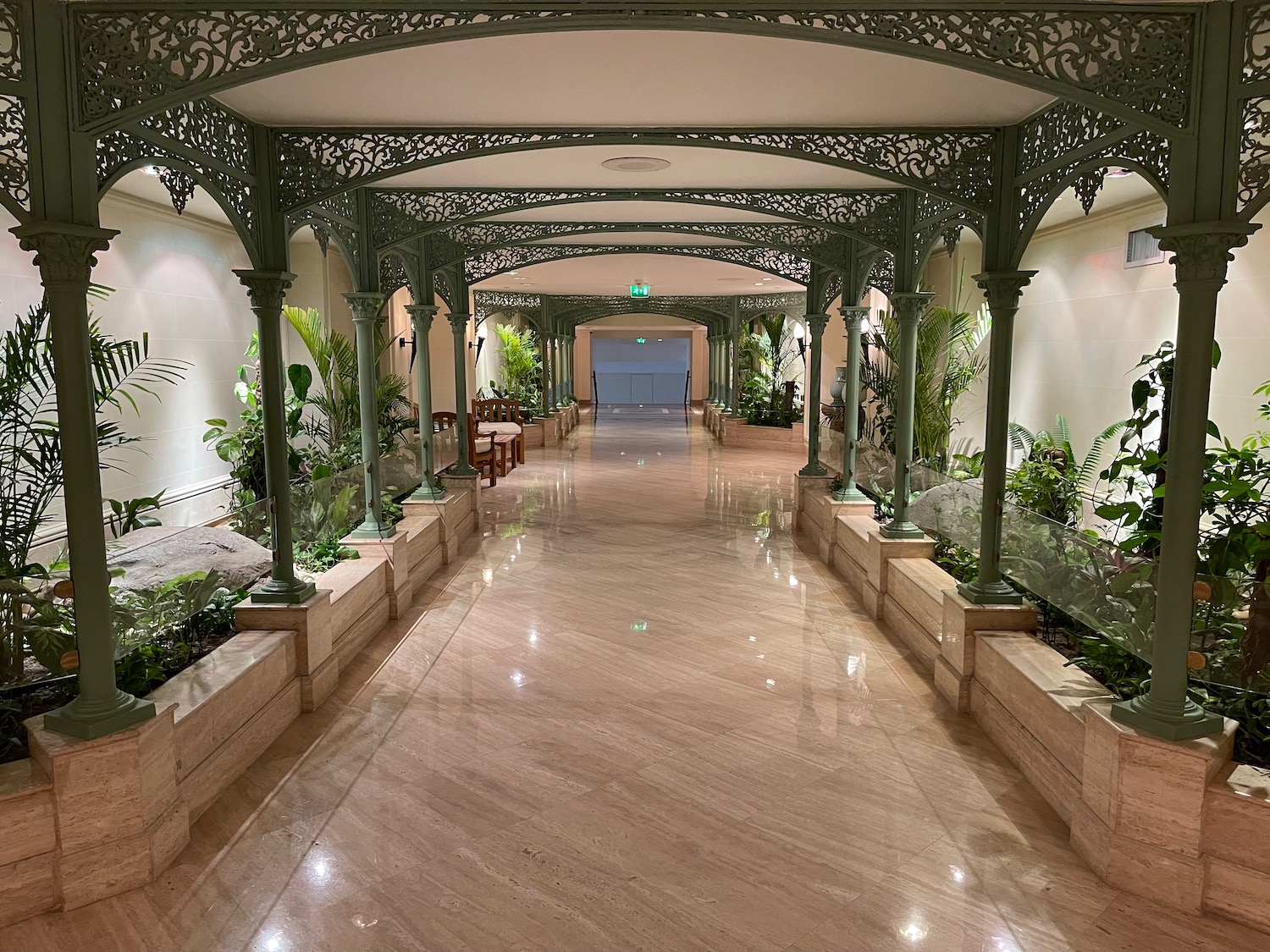 a long hallway with green pillars and plants