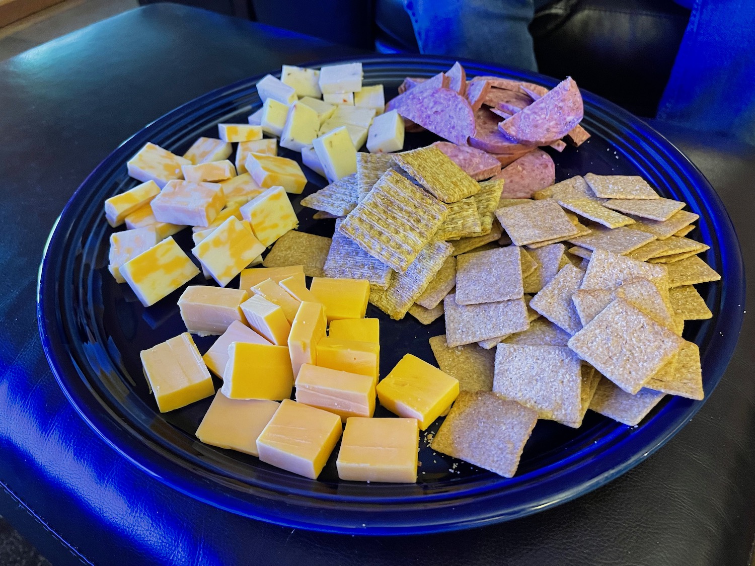 a plate of cheese crackers and salami on a black surface