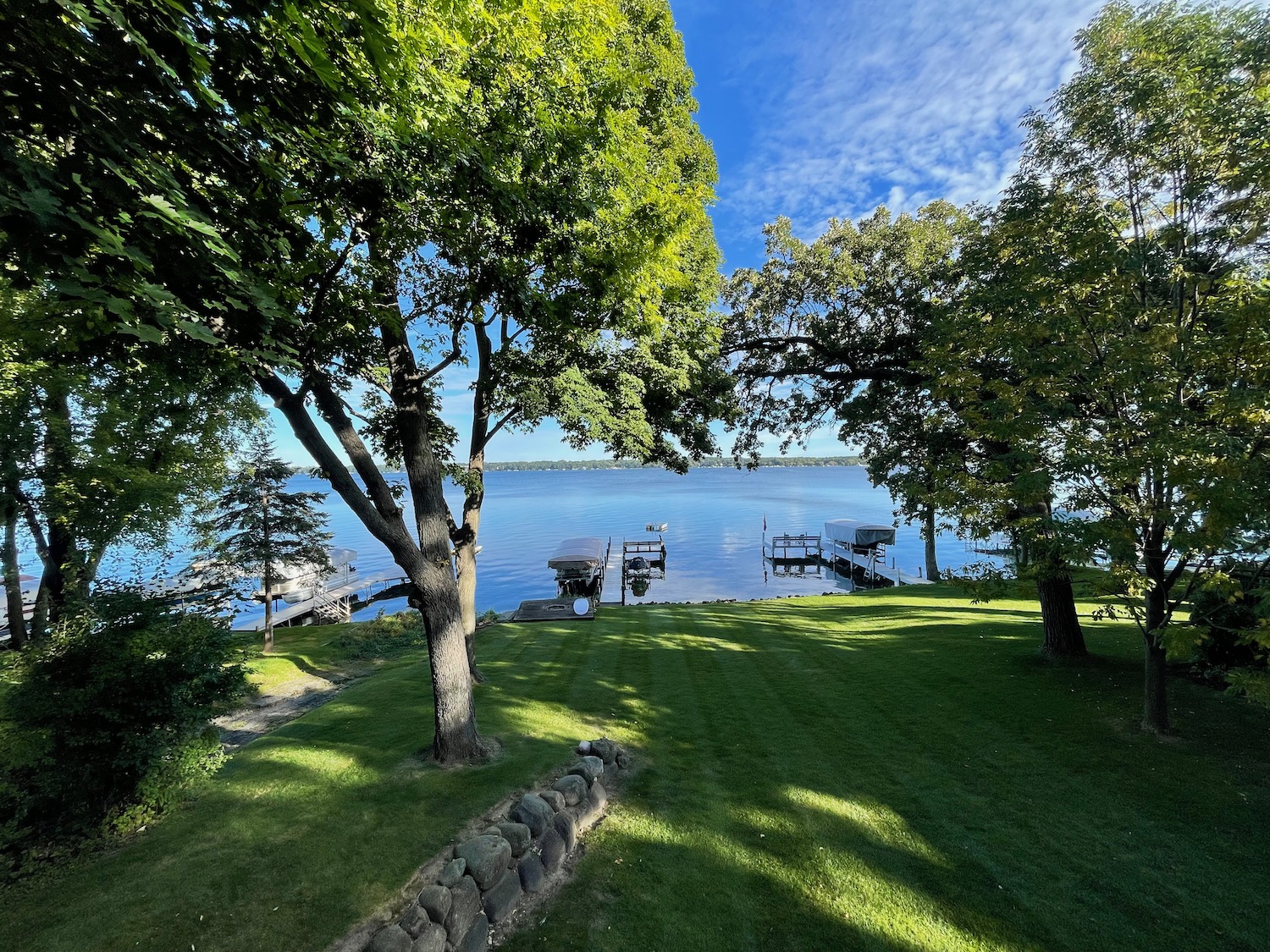 a lawn with trees and a dock on the water