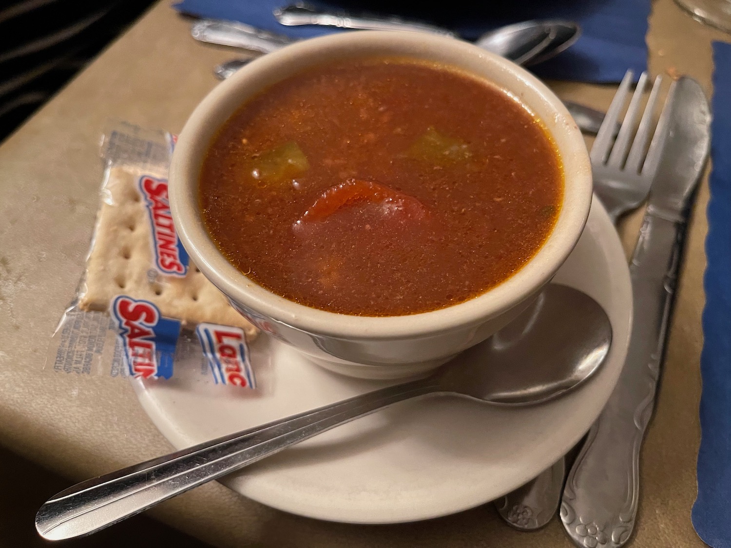a bowl of soup on a plate with spoon and crackers