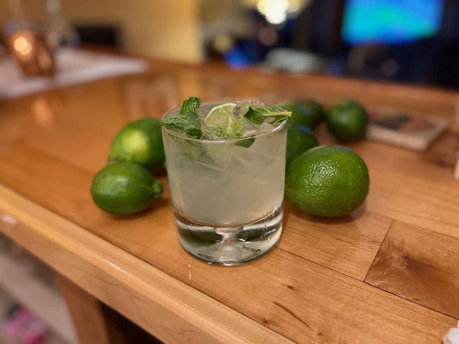 a glass of liquid with ice and limes on a table