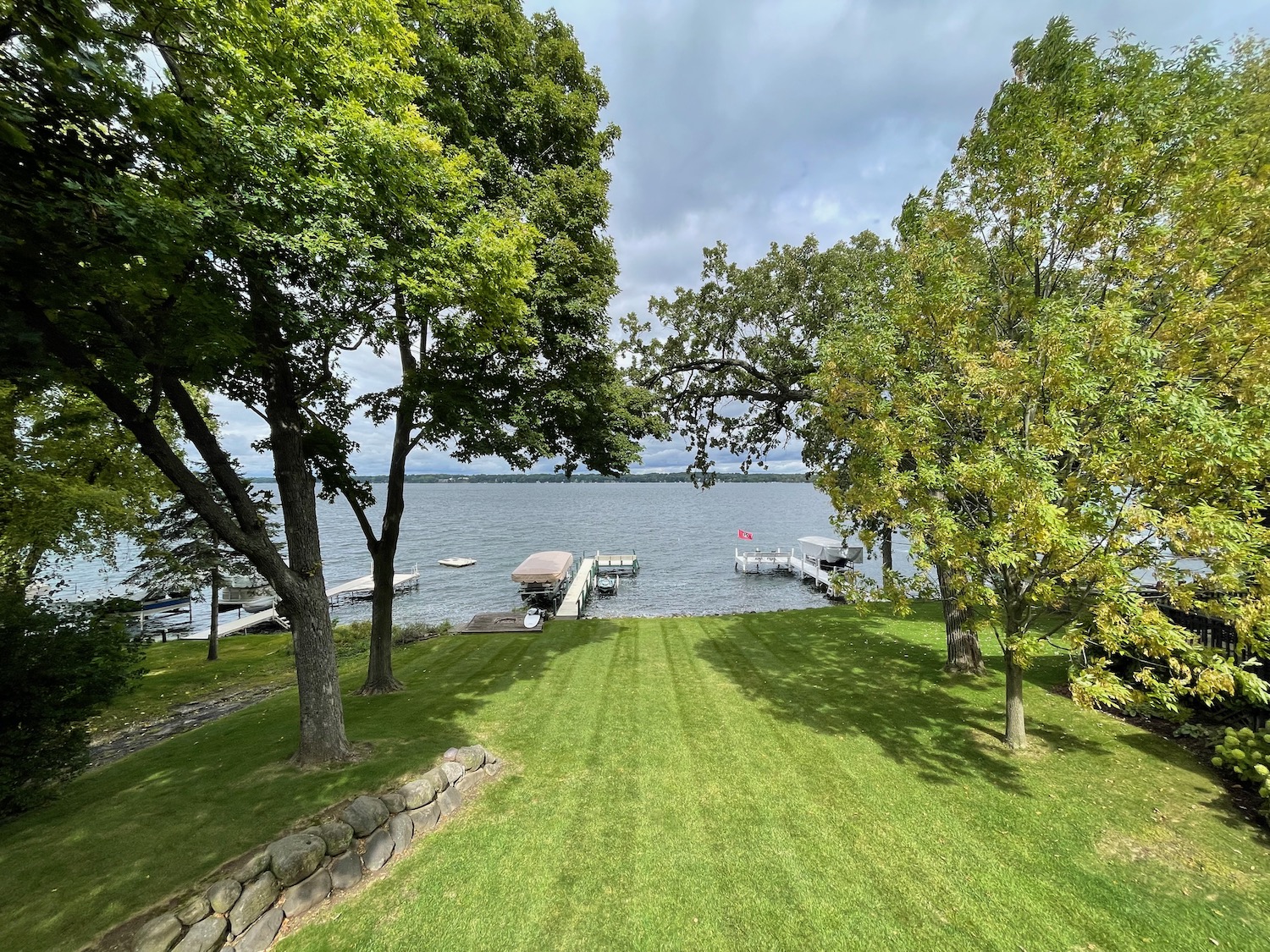 a grass lawn with trees and a dock on the water