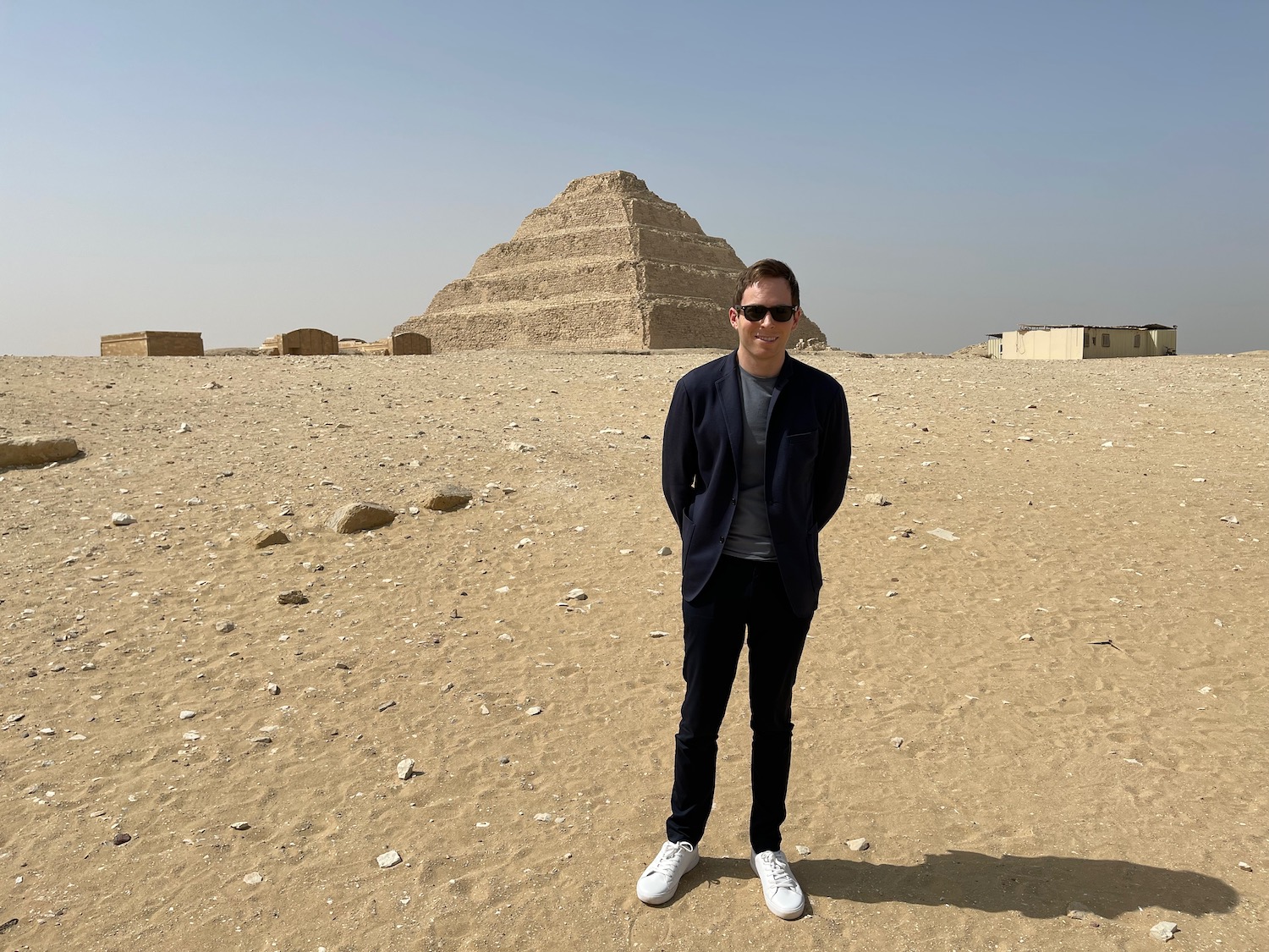 a man standing in a desert with a pyramid in the background