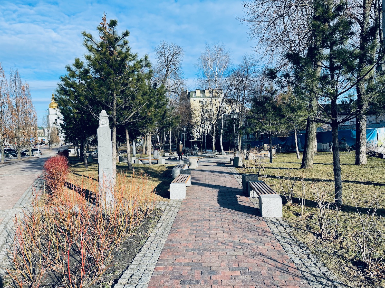 a brick path with benches and trees in the background