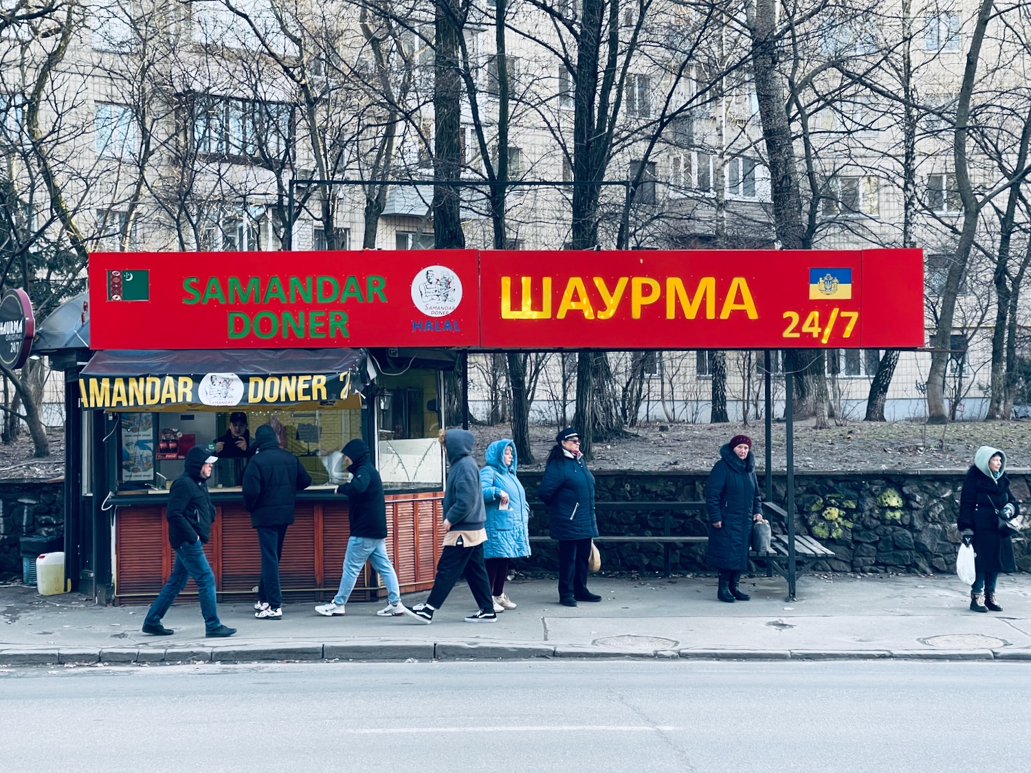 a group of people walking on a sidewalk next to a food stand