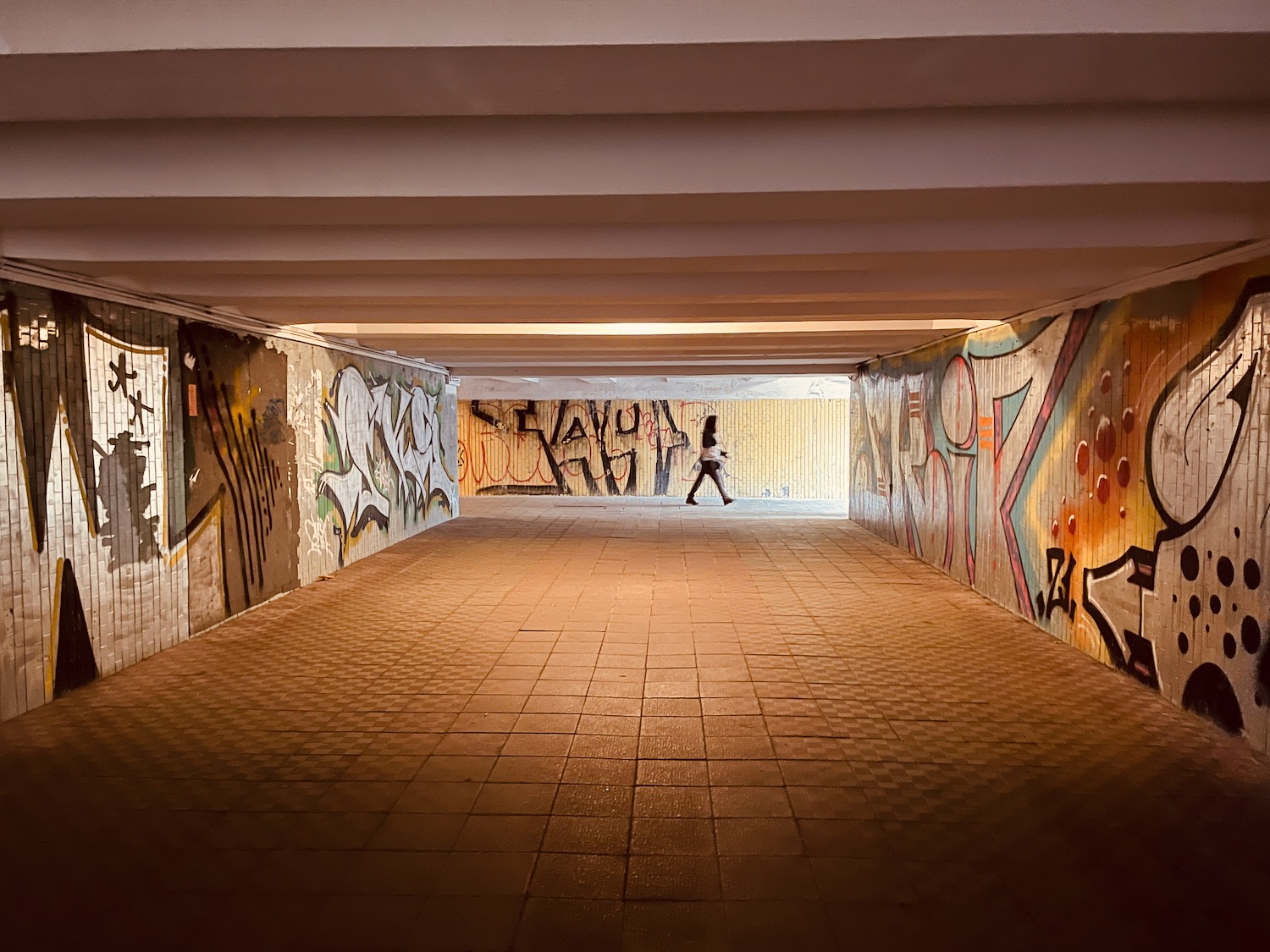 a person walking in a tunnel with graffiti on walls