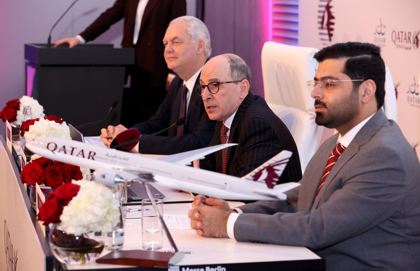 a group of men sitting at a table with a model airplane