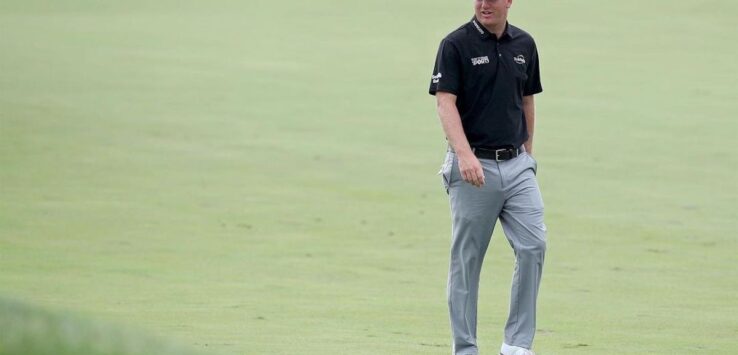 a man in a black shirt and grey pants walking on a golf course