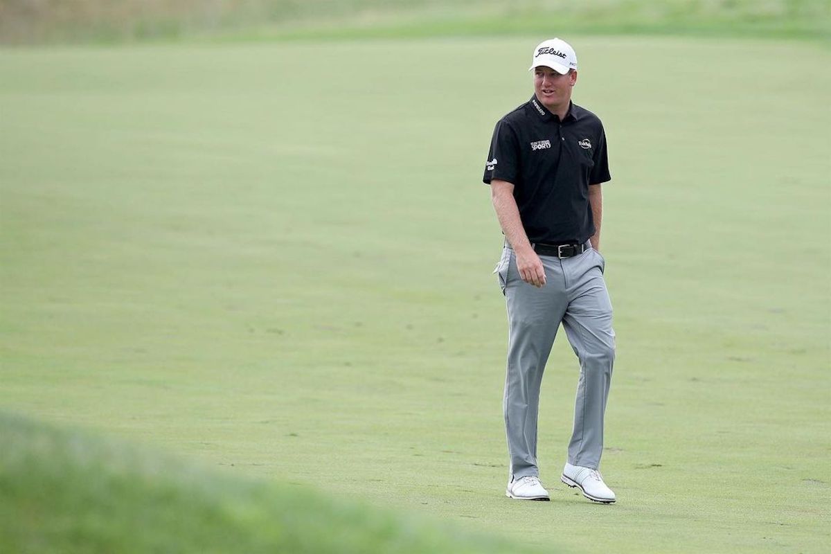 a man in a black shirt and grey pants walking on a golf course