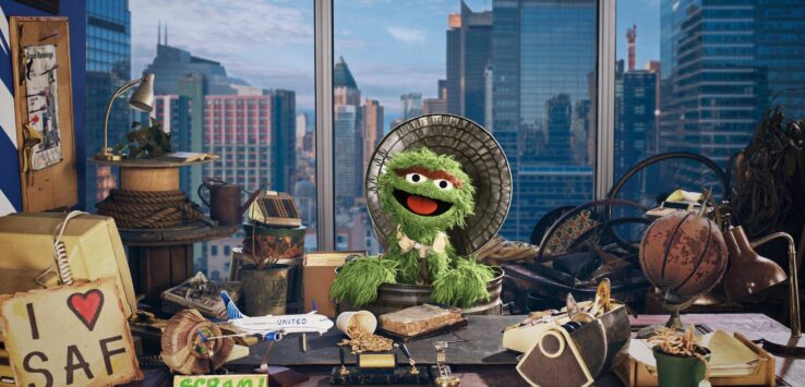 a green puppet in a room with a city view