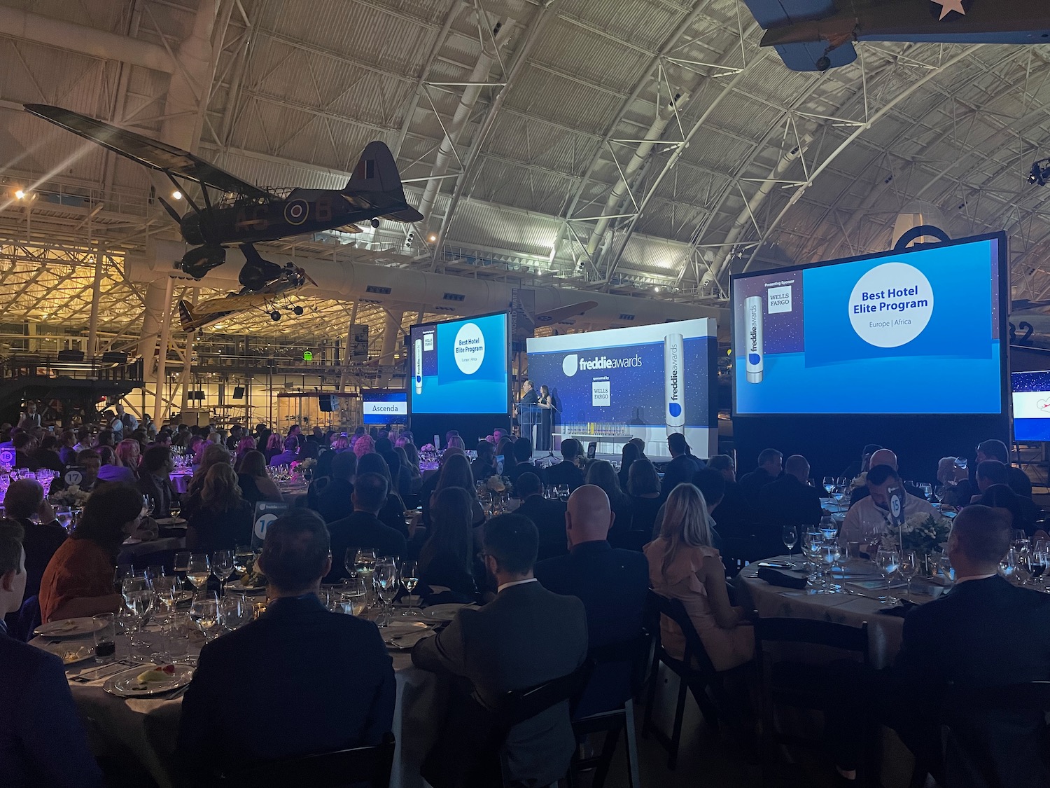 a group of people sitting at tables in a large room with large screens