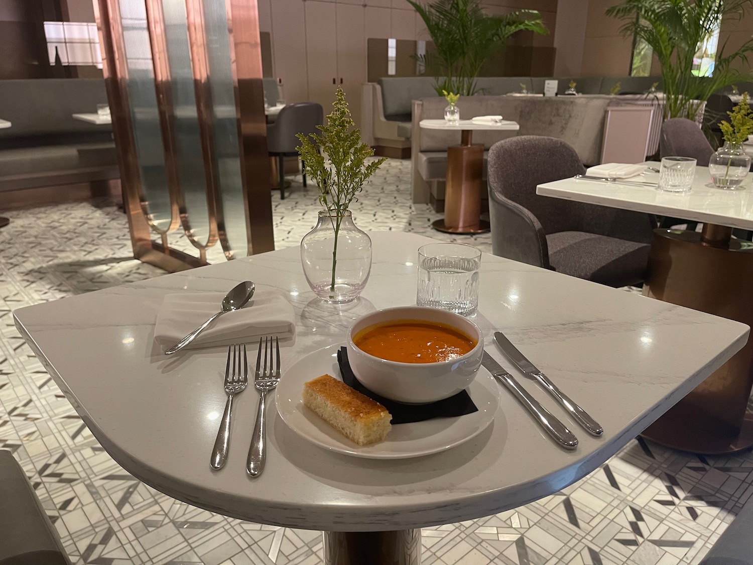 a bowl of soup on a white plate with bread and silverware on a table